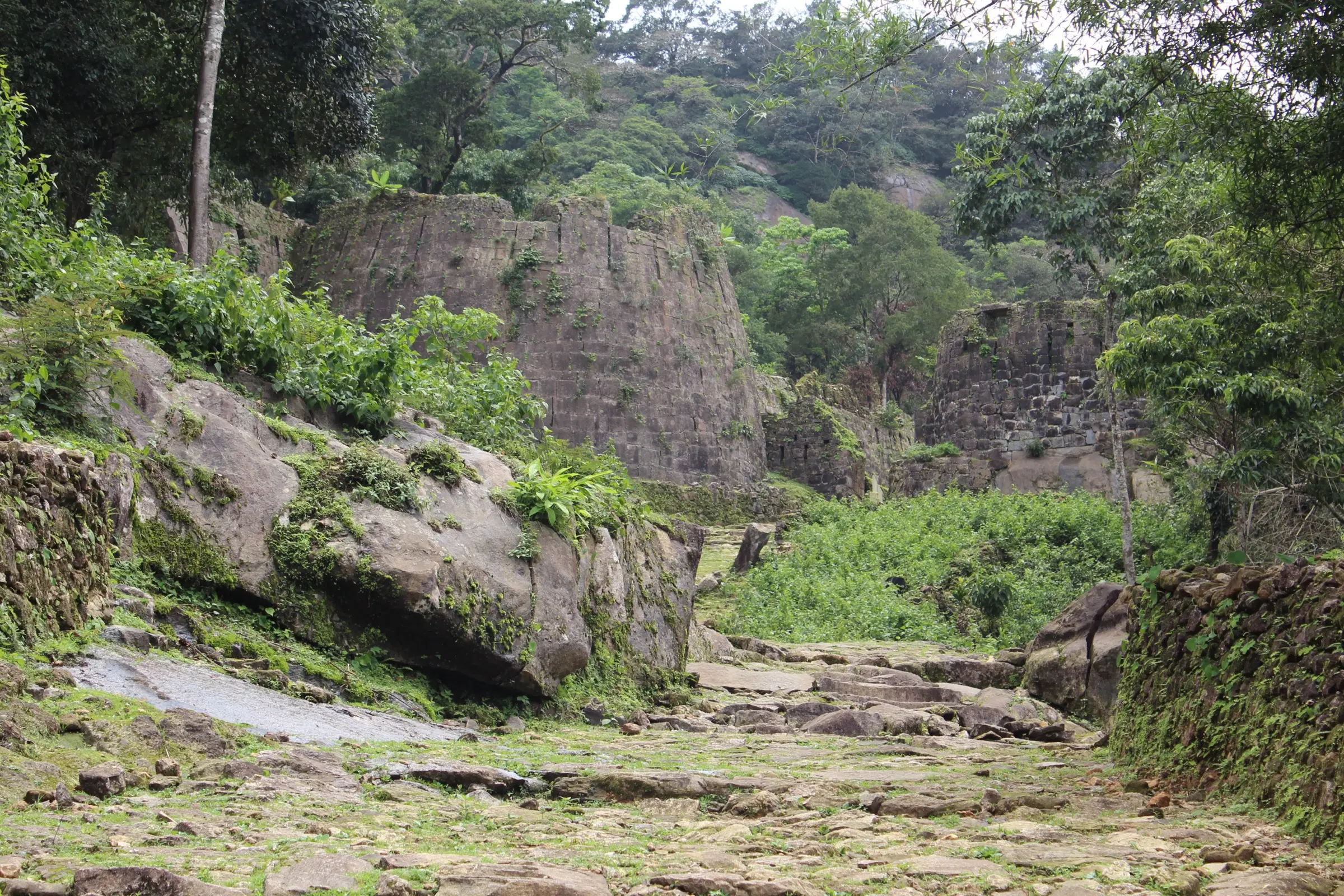 Stone-paved path climbing between boulders and a fort wall in the forest at Kavaledurga