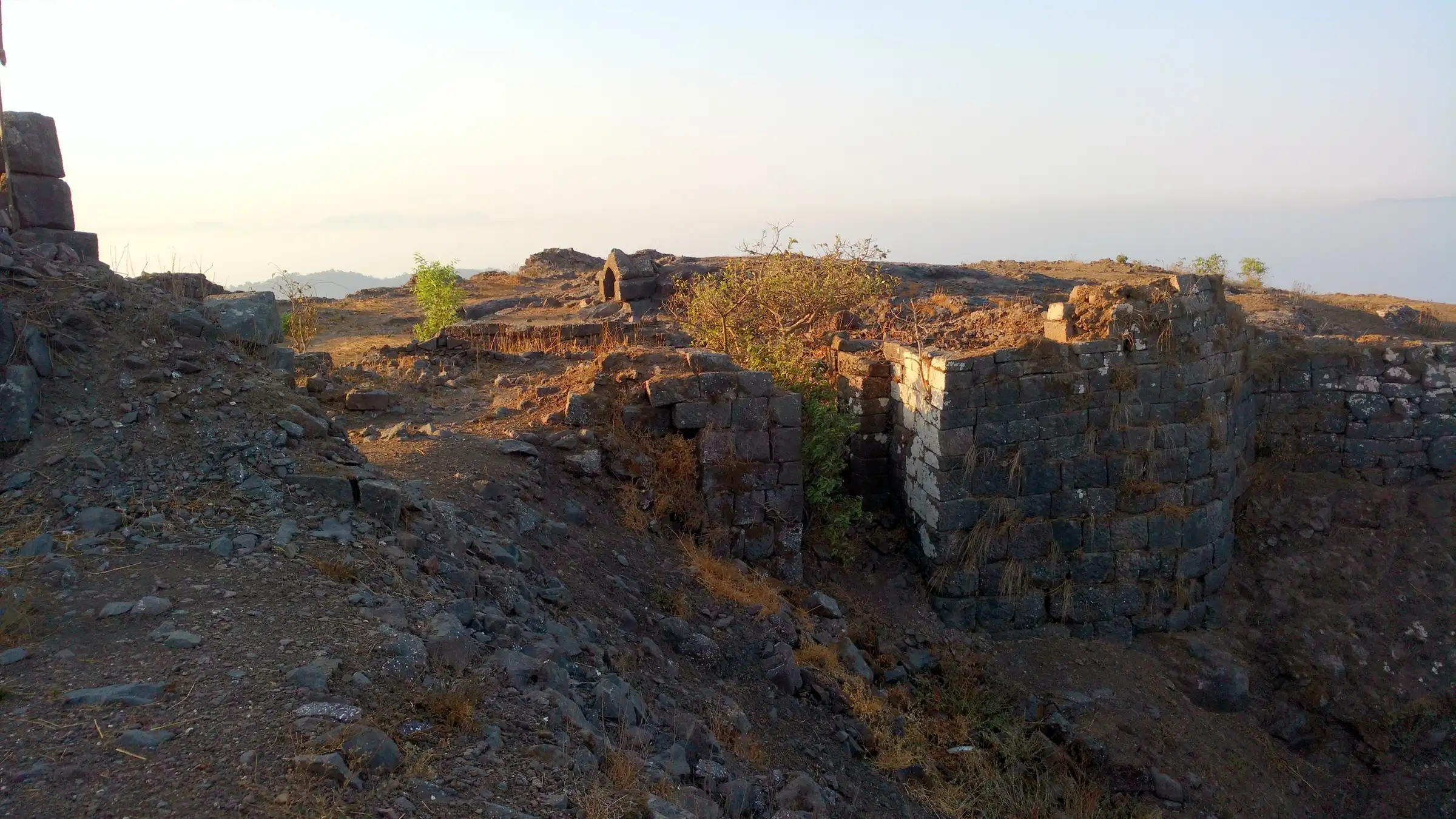 Ruined stone fortification and a bastion on Manikgad fort in early morning light