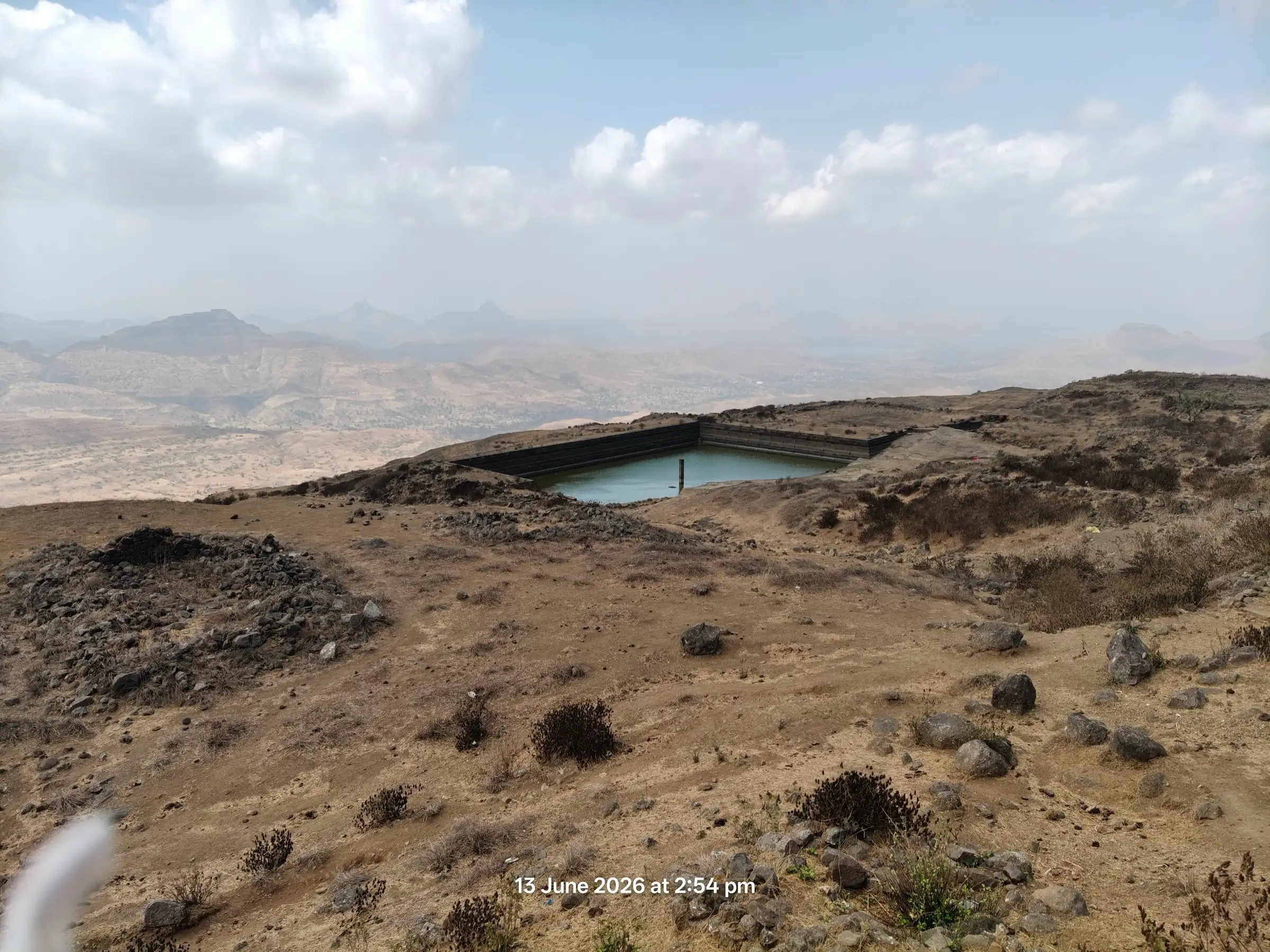 A rock-cut water tank on the dry, stony summit plateau of Salher fort with hazy hills beyond