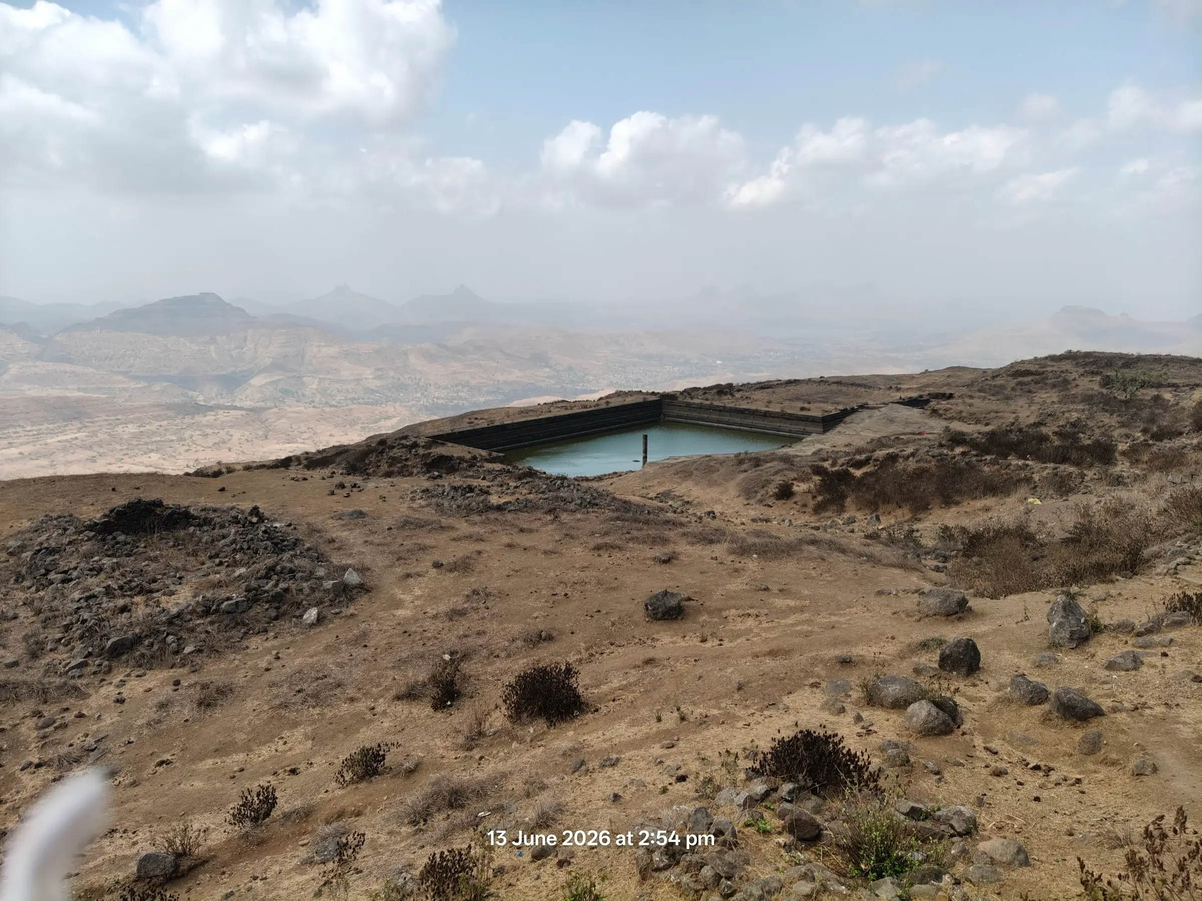 A rock-cut water tank on the dry, stony summit plateau of Salher fort with hazy hills beyond