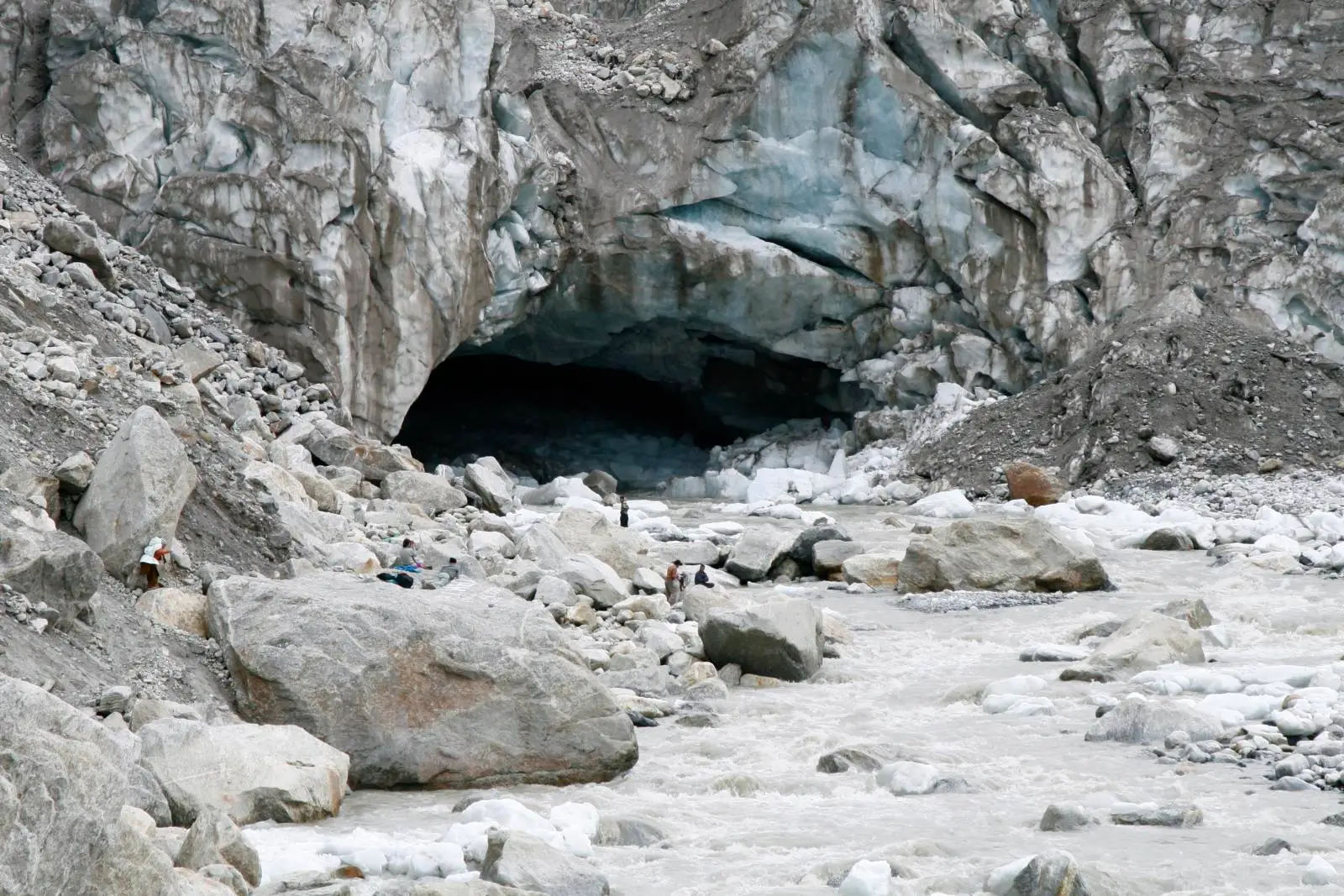 The dark ice cave at Gaumukh where the Bhagirathi flows out of the glacier, with pilgrims small among the boulders