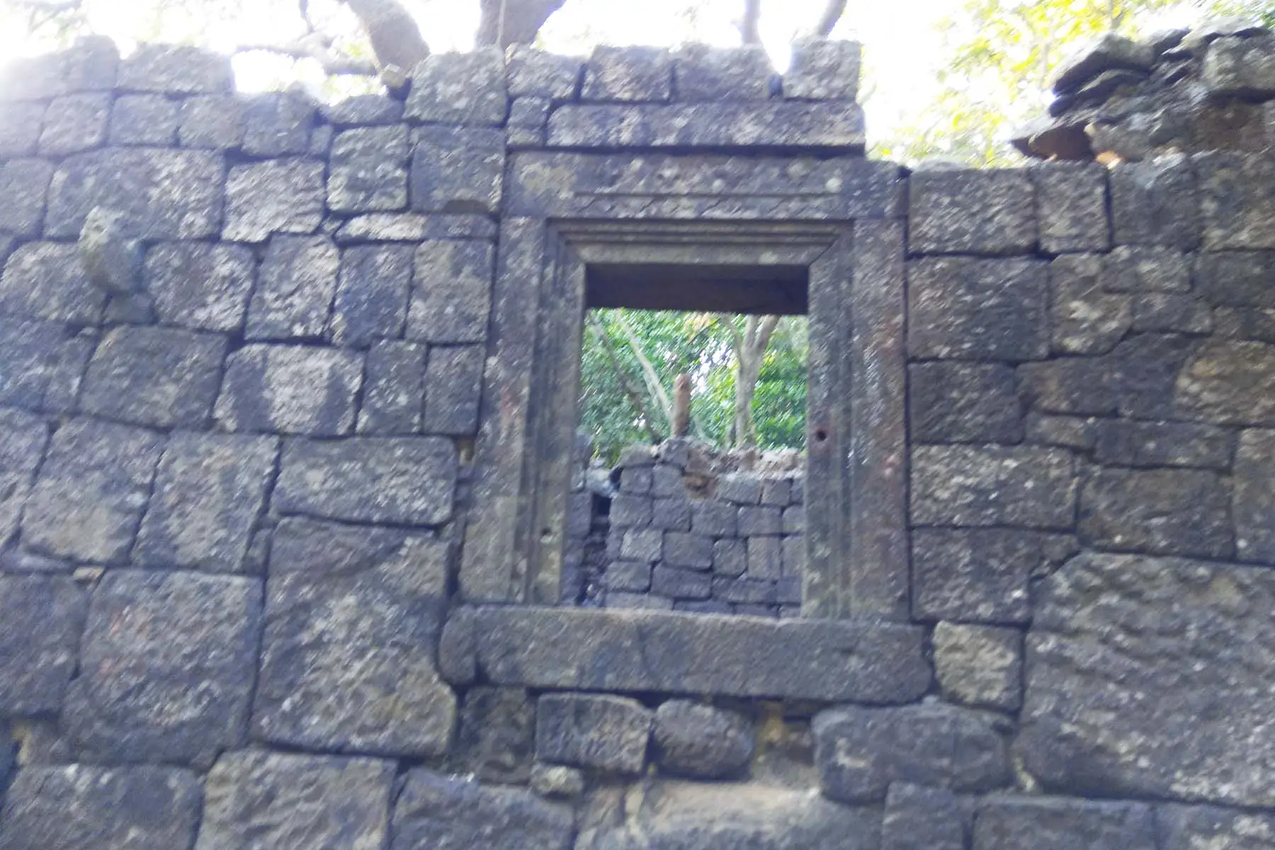 Dressed-stone wall with a carved window frame of one of the old buildings in the forest on Prabalgad