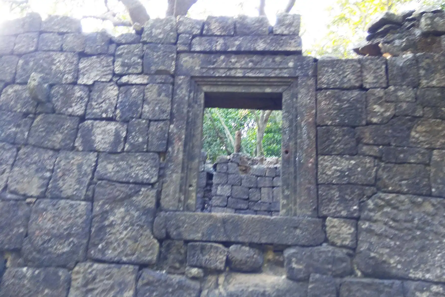 Dressed-stone wall with a carved window frame of one of the old buildings in the forest on Prabalgad