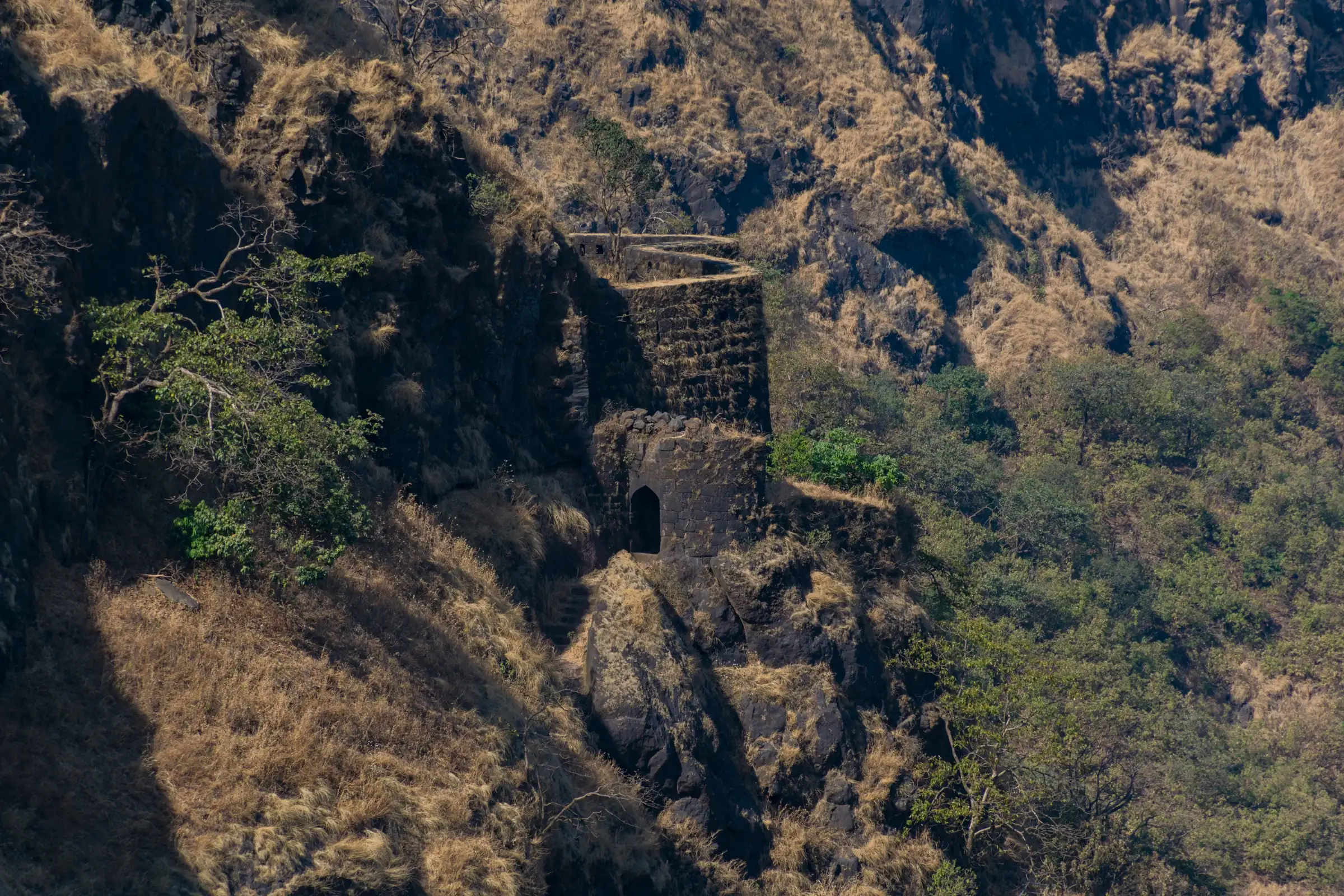 The stone Gunjavane Darwaza gateway and bastion set into a steep grassy cliff of Rajgad