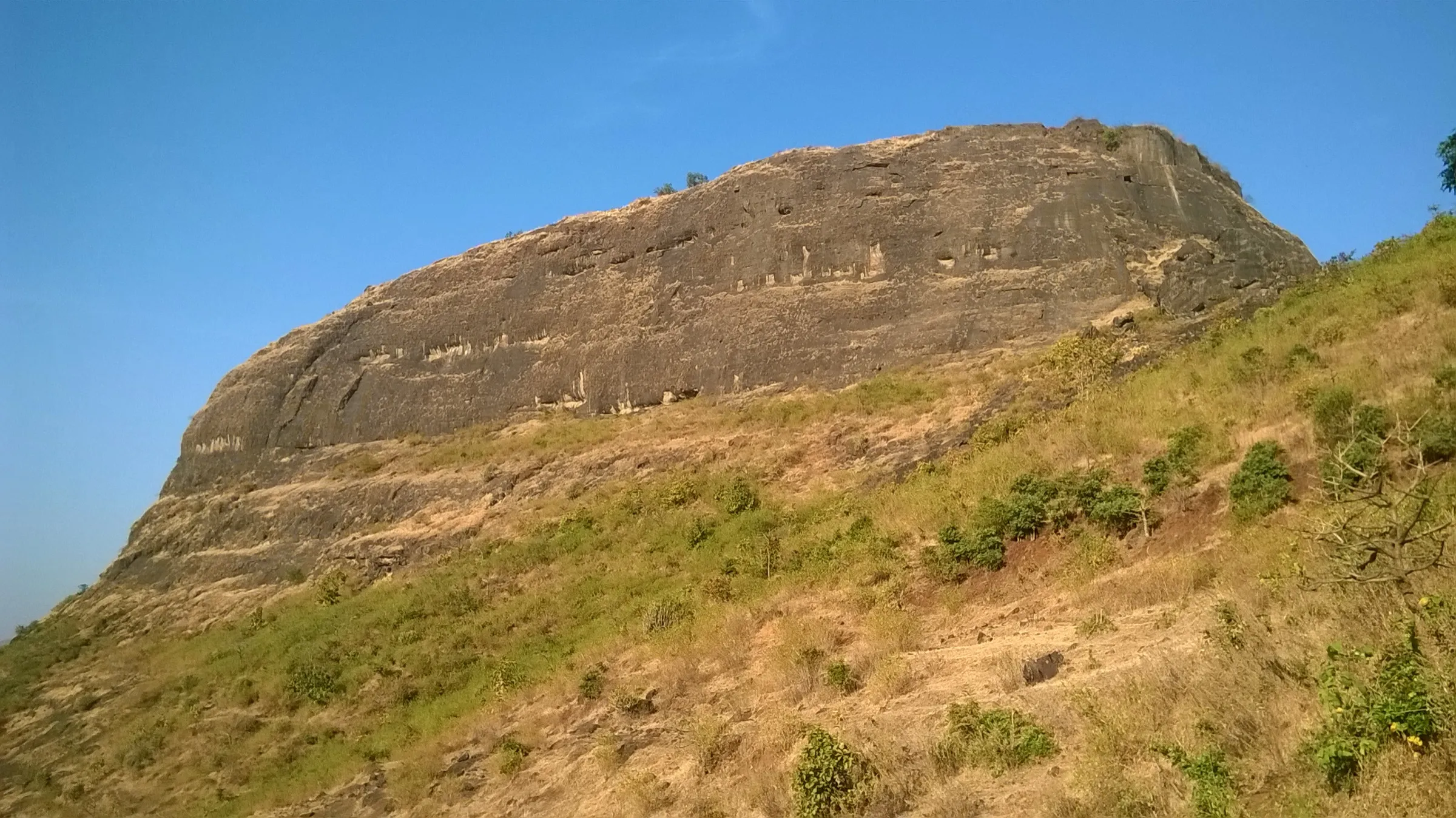 The sheer rock scarp of Hadsar Fort rising above grassy slopes under a clear blue sky