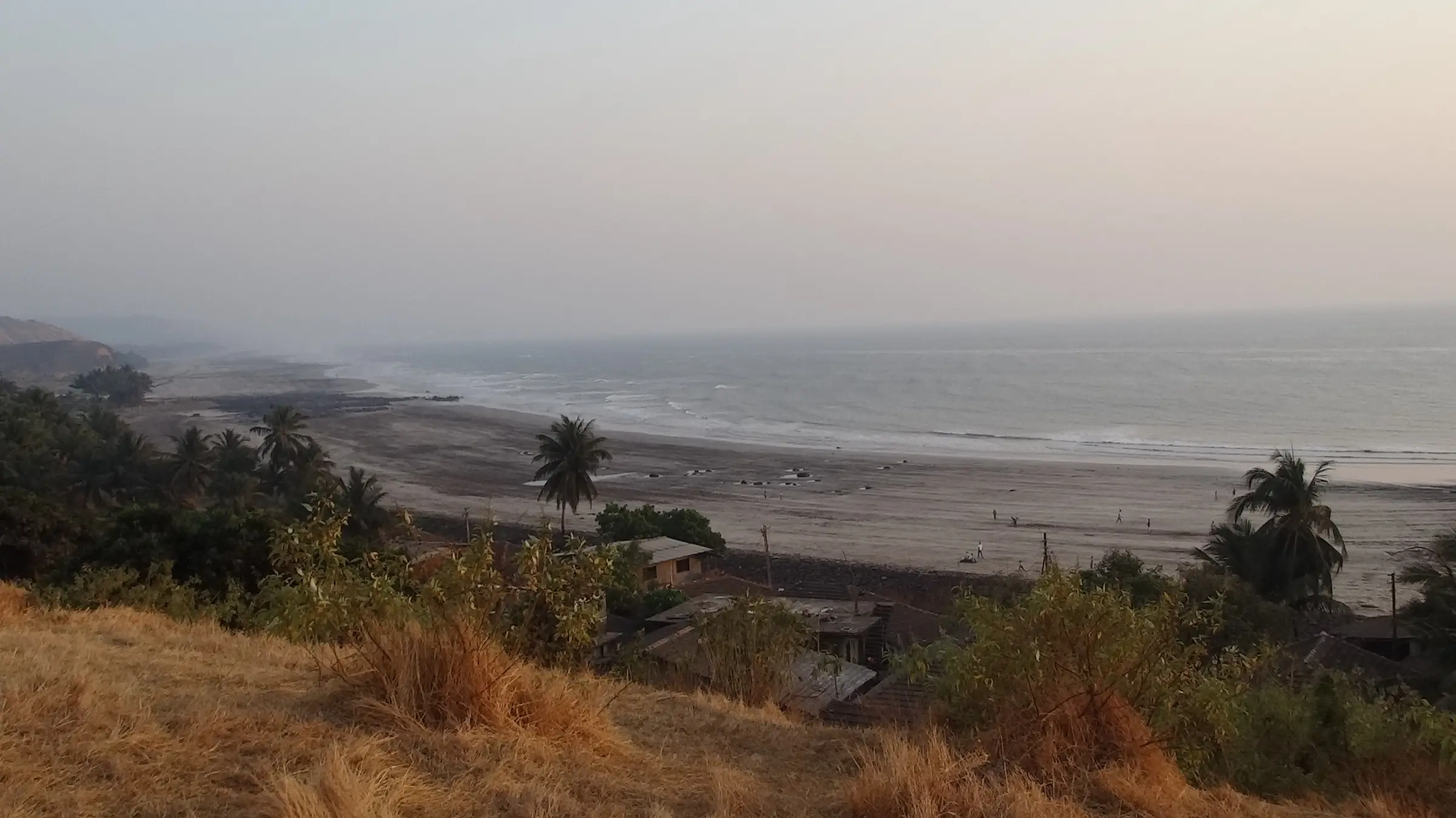 Harnai beach and village roofs seen from a dry grassy hilltop, with the coast stretching away in haze