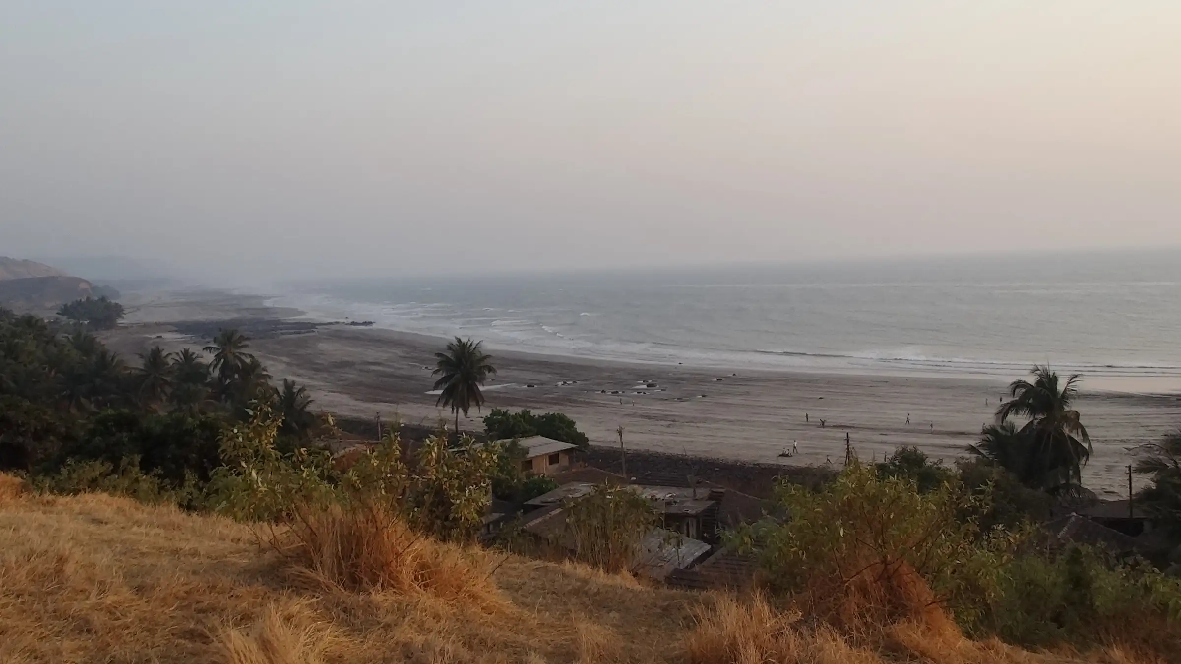 Harnai beach and village roofs seen from a dry grassy hilltop, with the coast stretching away in haze
