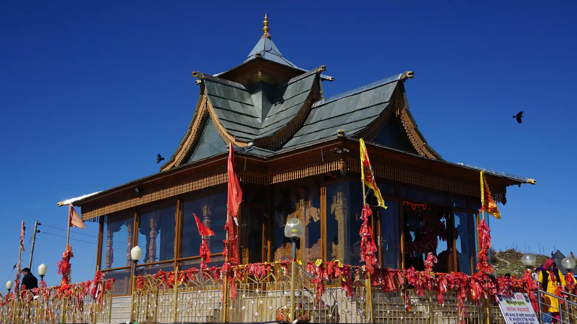 The wooden pagoda-roofed Hatu Mata temple with red chunris tied on its railings under a clear blue sky