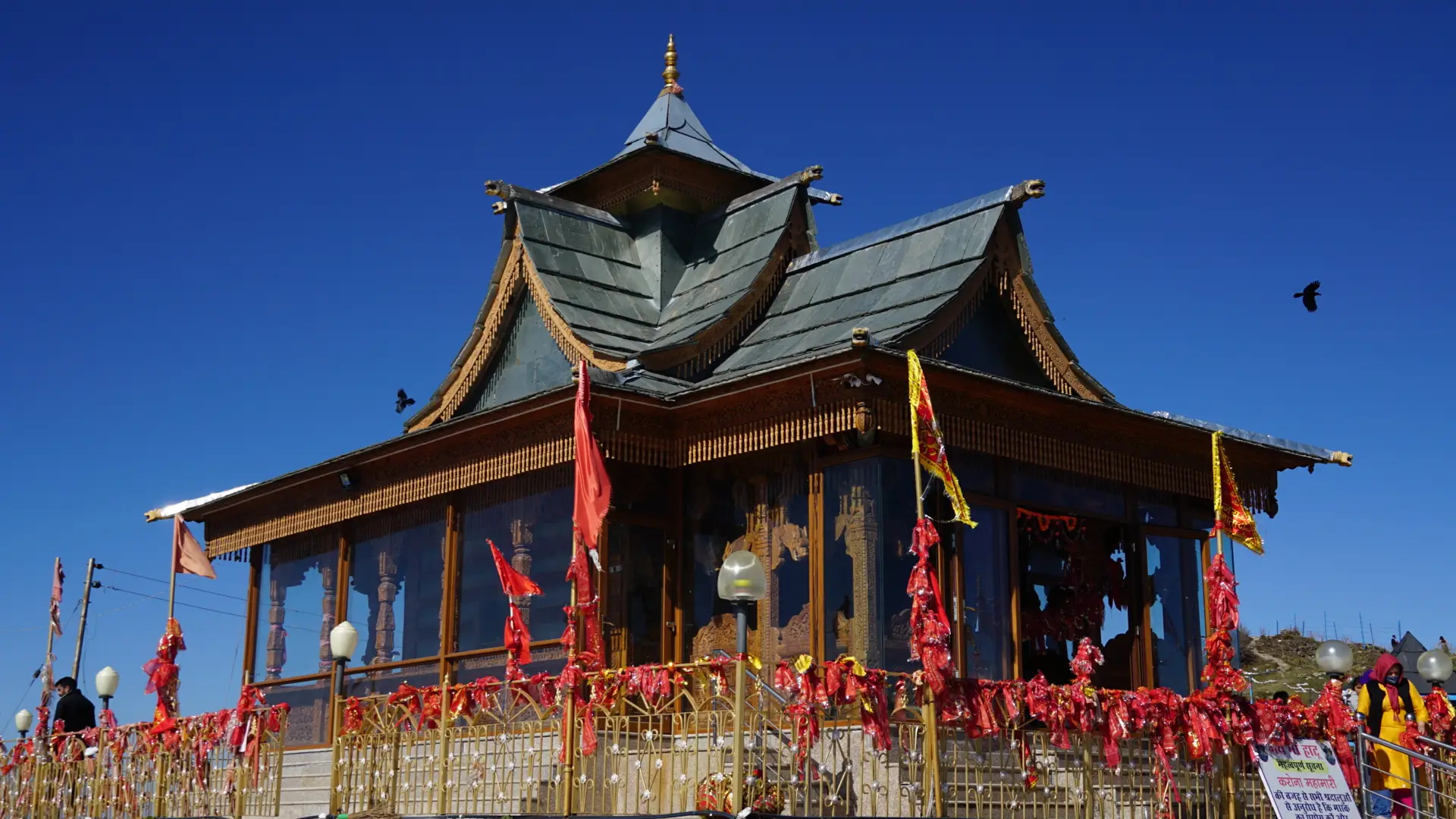 The wooden pagoda-roofed Hatu Mata temple with red chunris tied on its railings under a clear blue sky