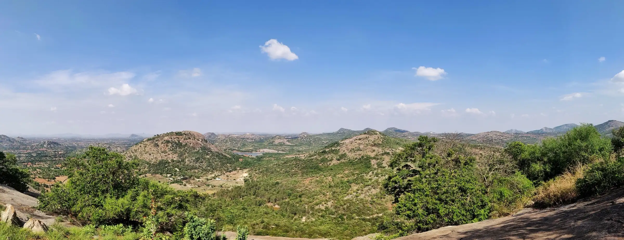 Panorama of scrub-covered granite hills and a small lake from Avalabetta, a neighbouring hill seen from the Varlakonda summit. This is the surrounding area, not the Varlakonda trail itself