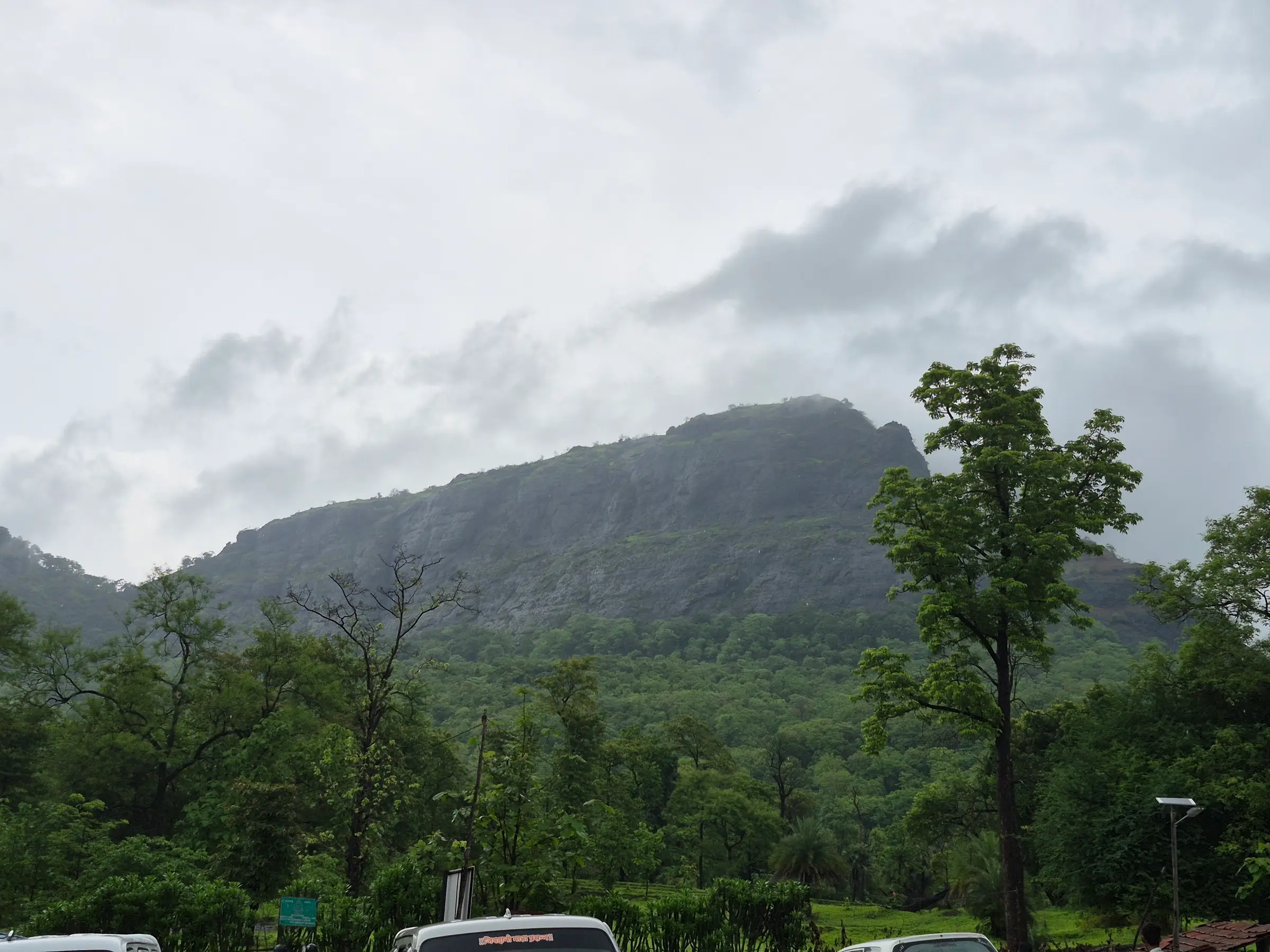 The forested cliffs of Asheri fort under monsoon clouds, seen from the base near Khodkona