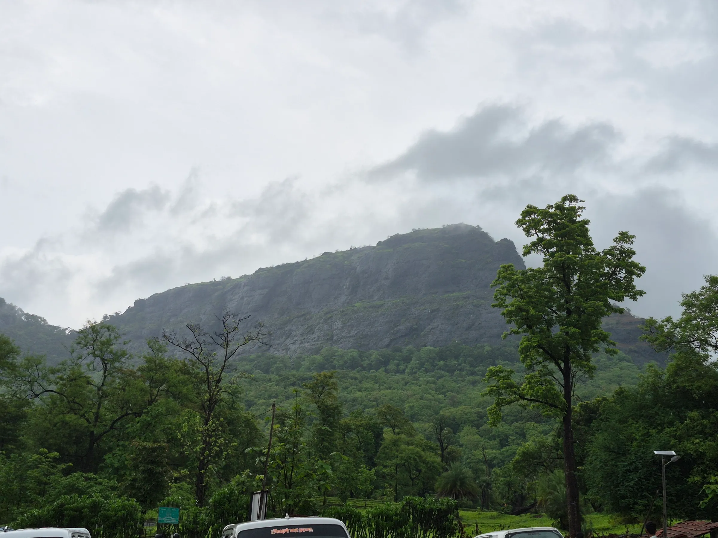 The forested cliffs of Asheri fort under monsoon clouds, seen from the base near Khodkona