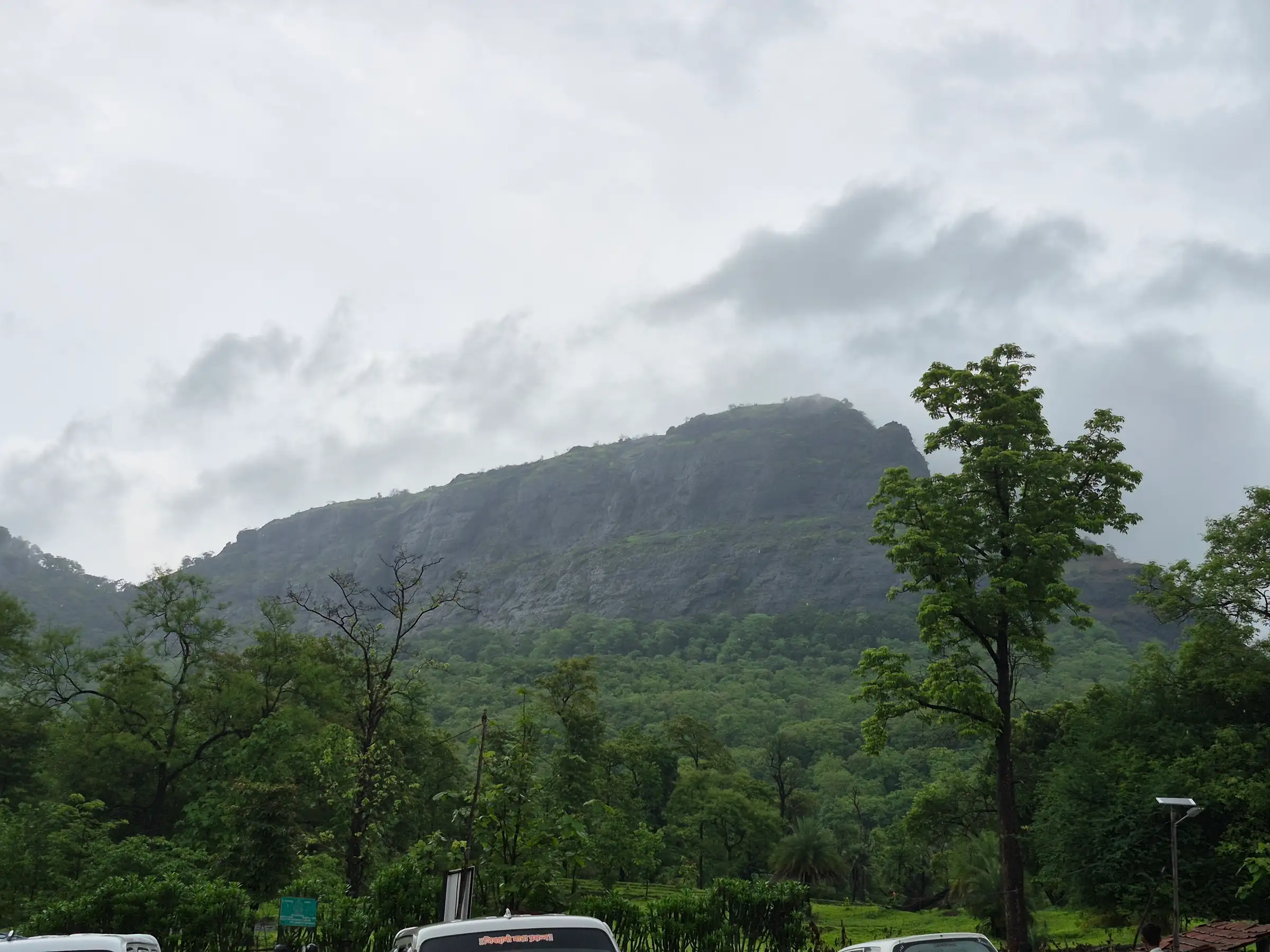 The forested cliffs of Asheri fort under monsoon clouds, seen from the base near Khodkona