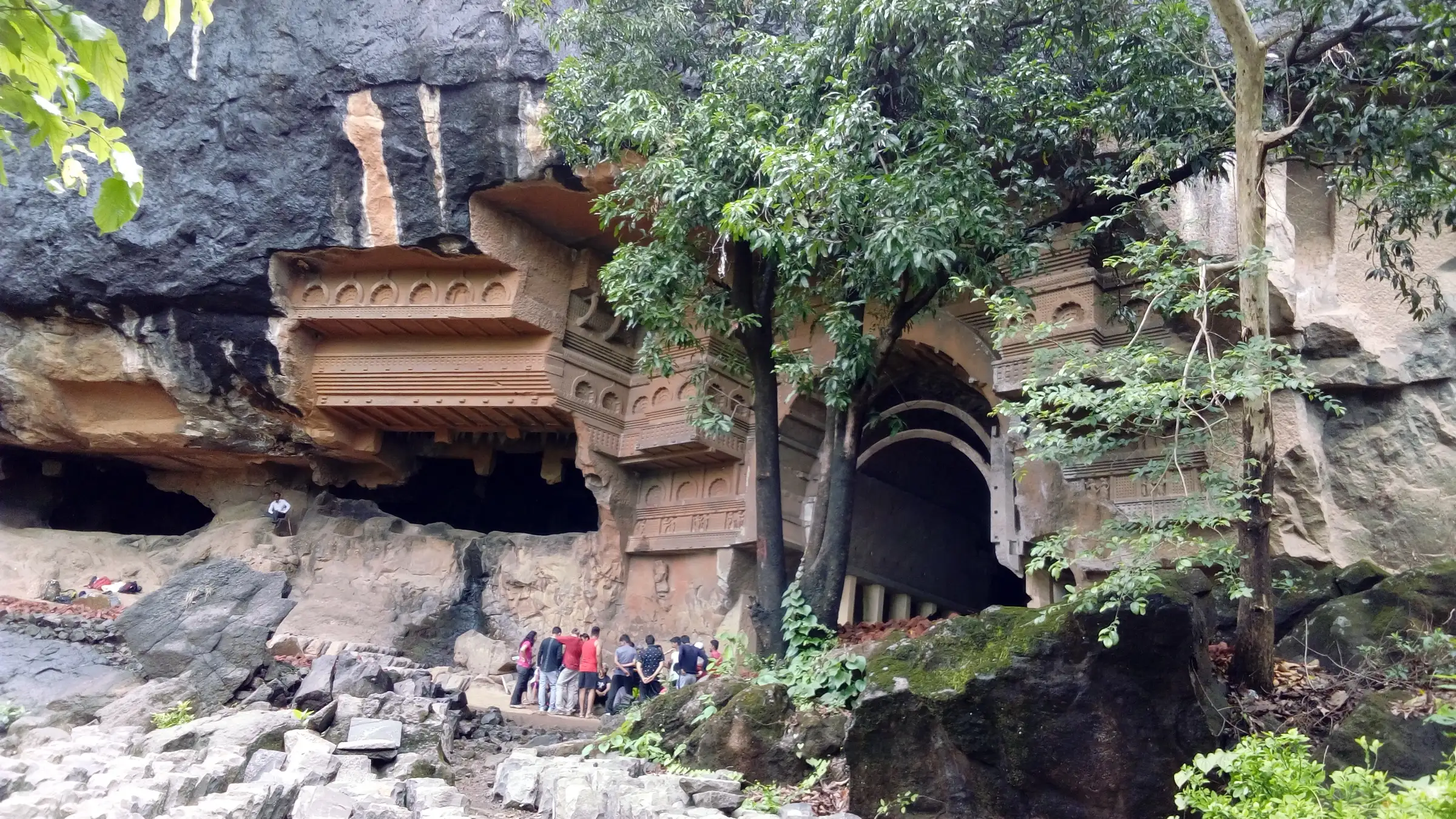 Kondana Caves carved into a basalt cliff, with the chaitya arch, carved facade and visitors at the foot of the rock