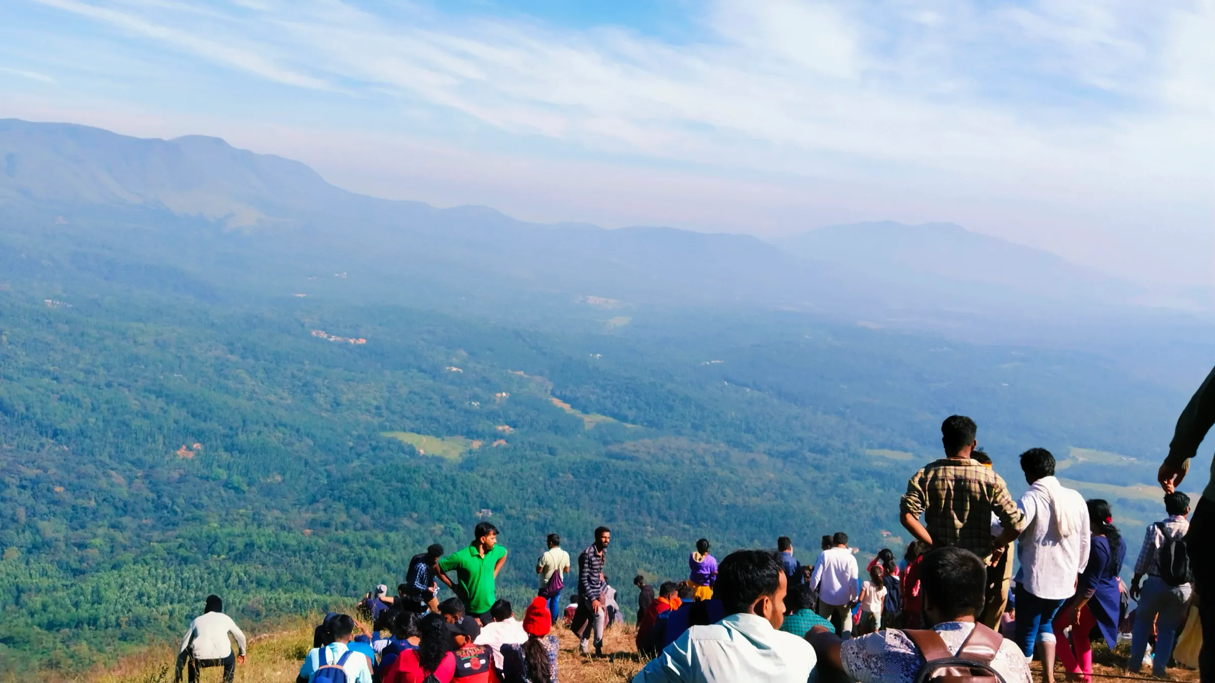 Pilgrims resting on the grassy top of Deviramma Betta above forested valleys and the Chandradrona hills on Deepavali morning