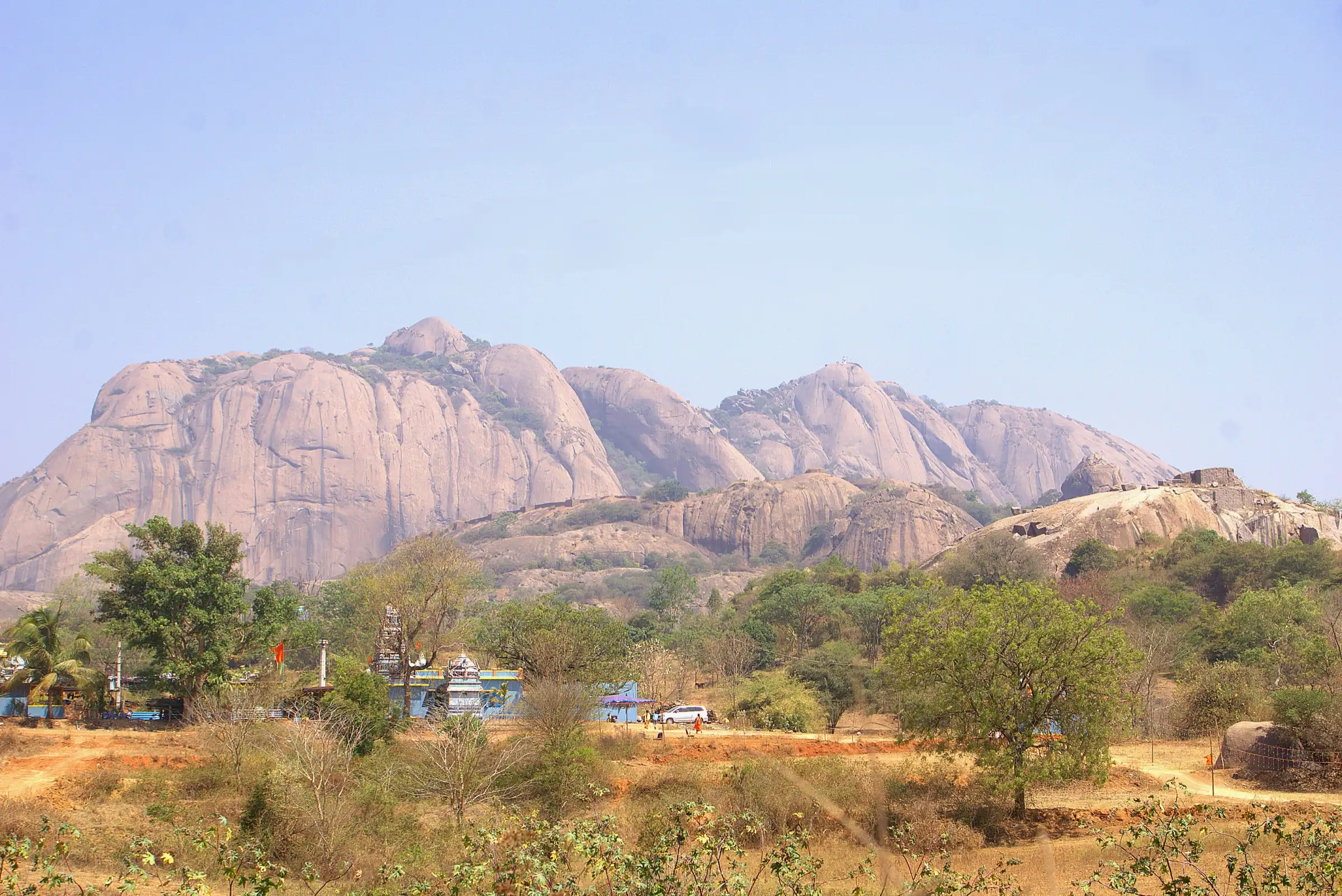 The pink granite domes of Savandurga hill rising above scrub forest and village houses, seen from the south