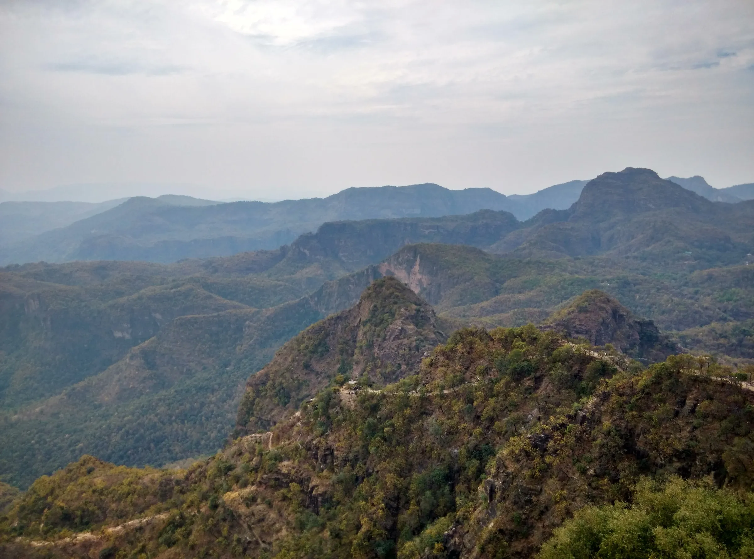 Forested Satpura ridges and rocky peaks seen from the top of Chauragarh, with the pilgrim trail winding along the ridge below