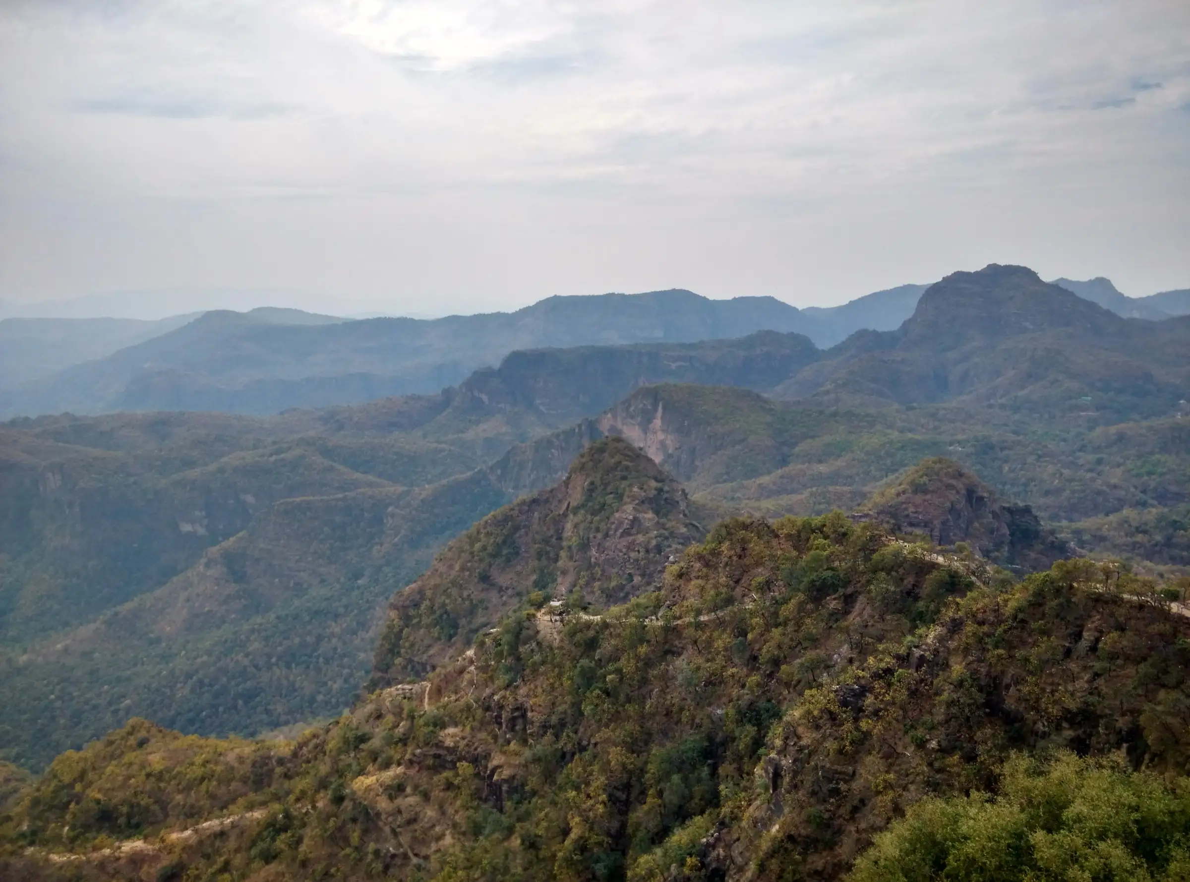 Forested Satpura ridges and rocky peaks seen from the top of Chauragarh, with the pilgrim trail winding along the ridge below