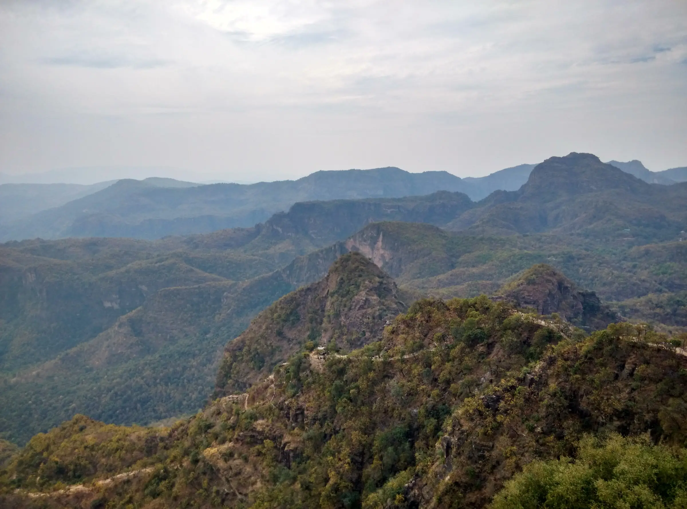 Forested Satpura ridges and rocky peaks seen from the top of Chauragarh, with the pilgrim trail winding along the ridge below