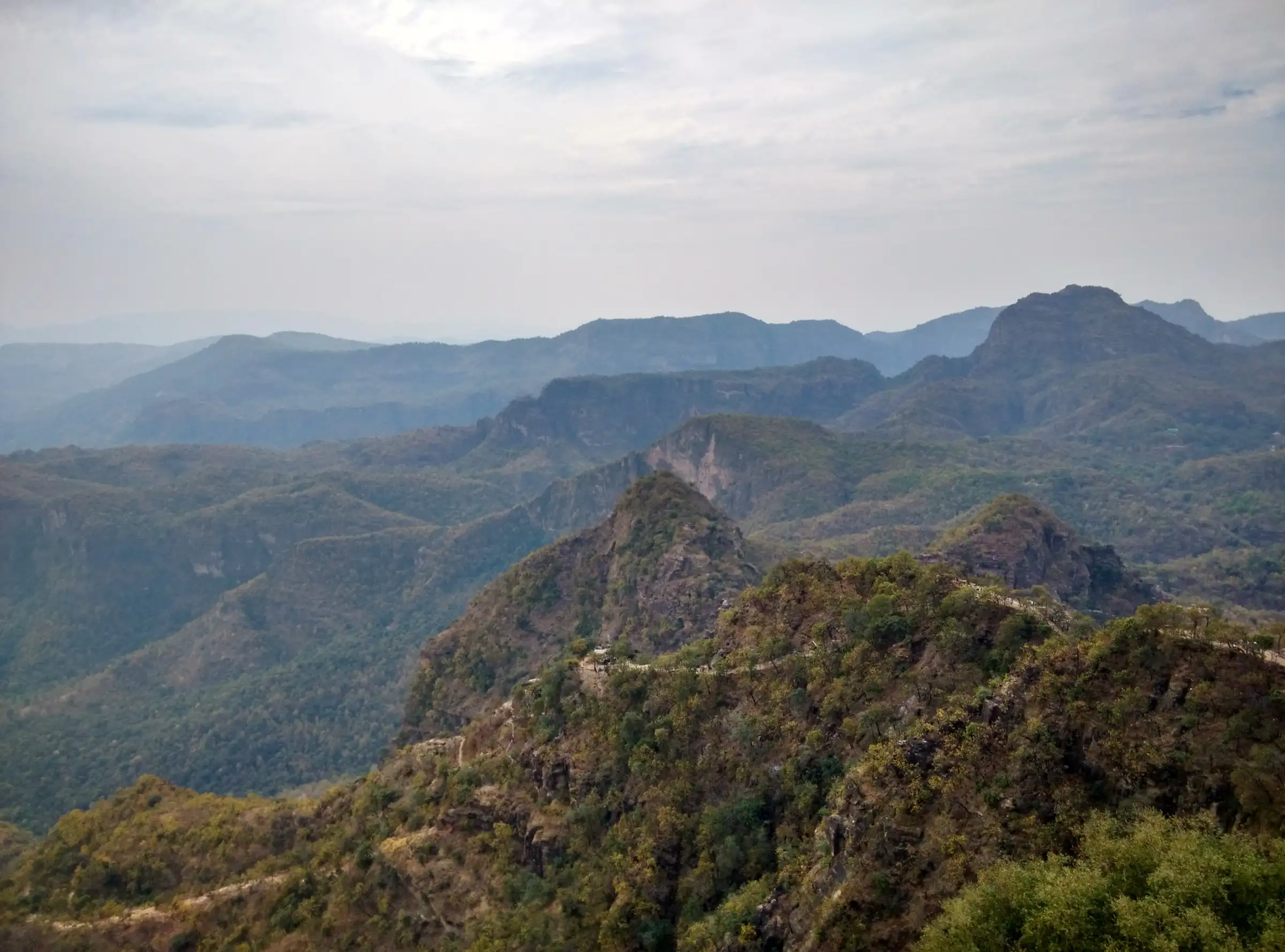 Forested Satpura ridges and rocky peaks seen from the top of Chauragarh, with the pilgrim trail winding along the ridge below