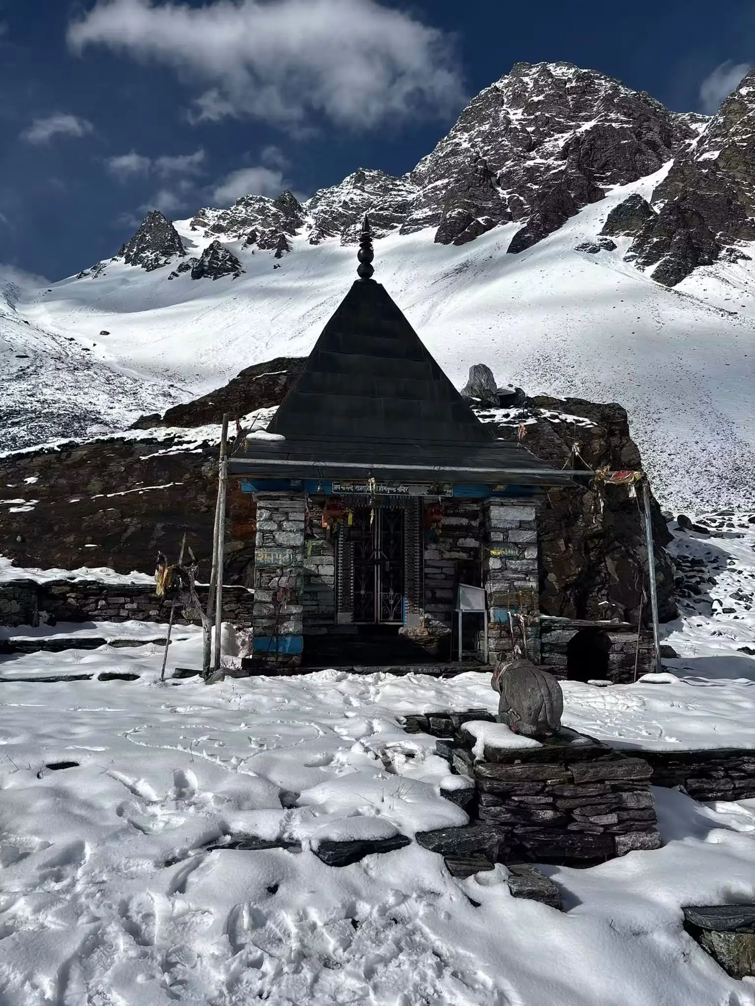 Small stone temple of Maa Nanda at Homkund in fresh snow below rocky snow-covered peaks