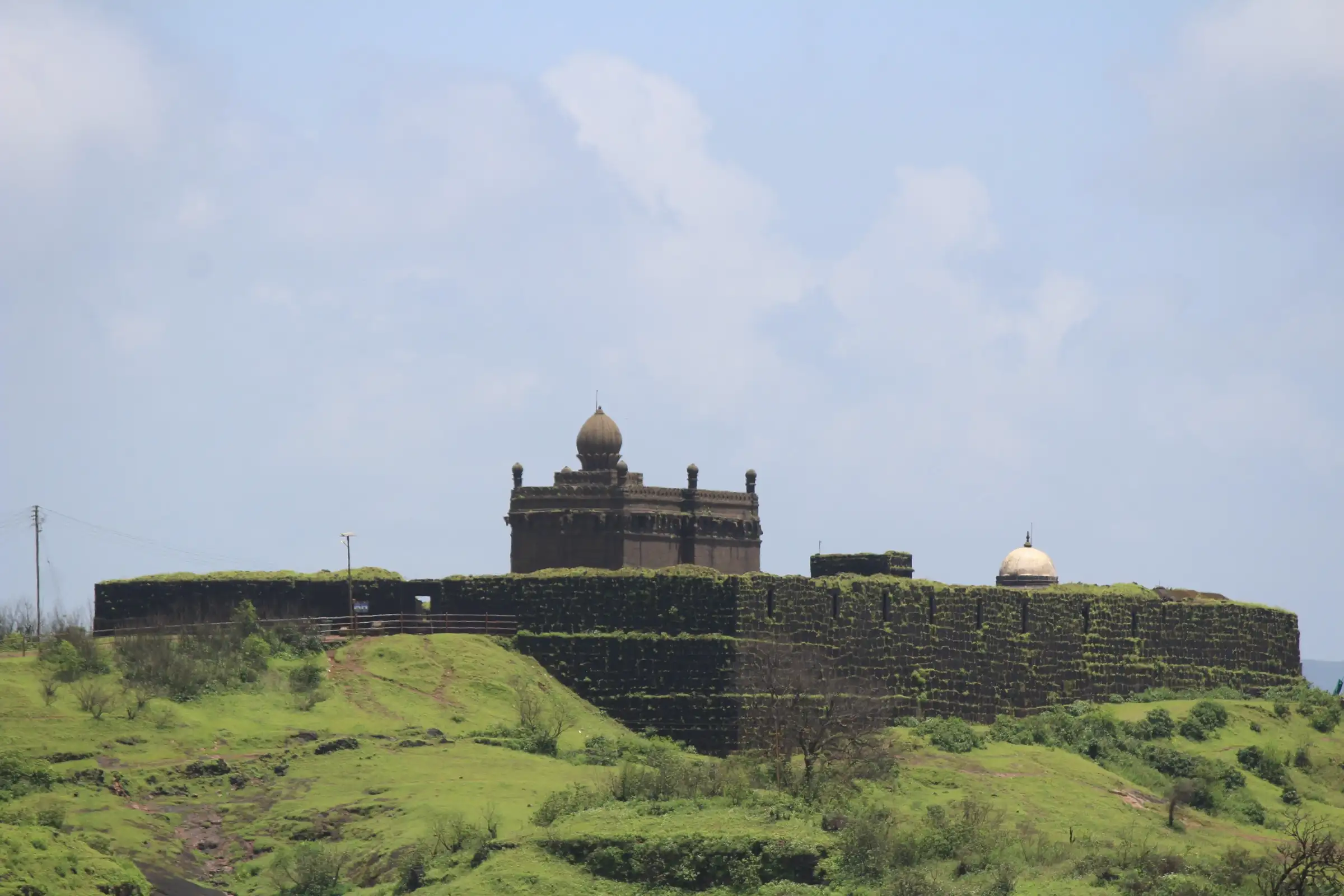 The stone Jagdishwar Mandir with its domed shikhar inside a walled enclosure on Raigad's grassy top