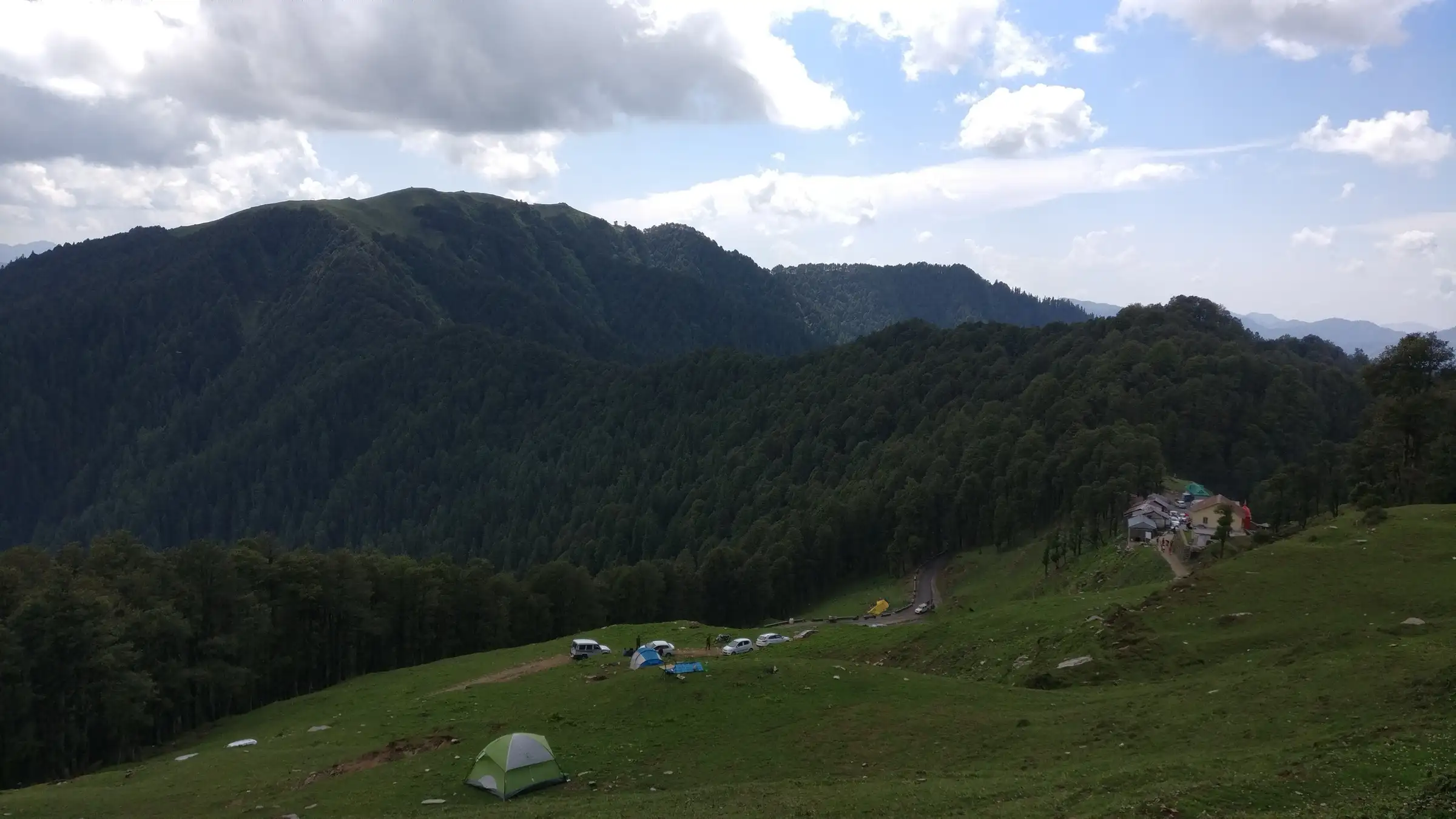 Grassy meadow with tents at Jalori Pass, the road and roadside dhabas below forested ridges