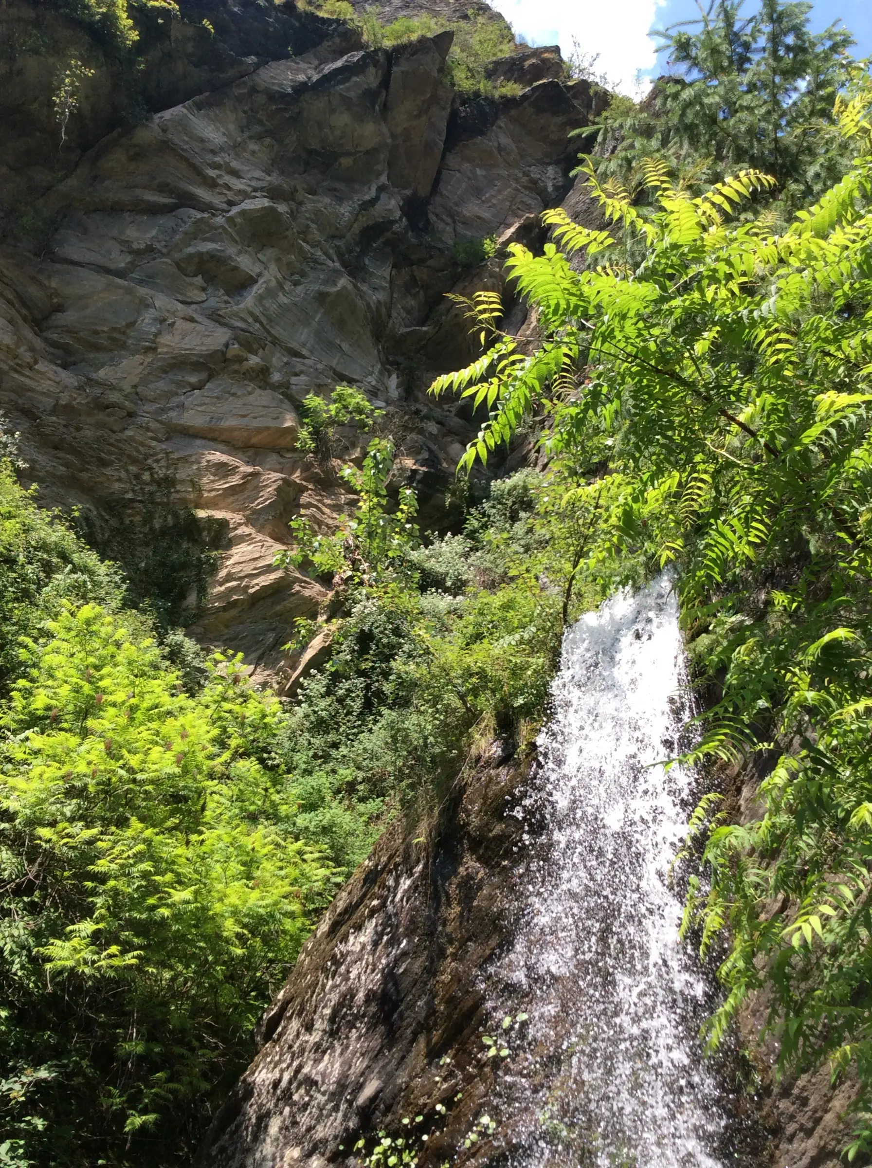Jana waterfall pouring down a rock face among green shrubs, passed early on the walk out of Jana village