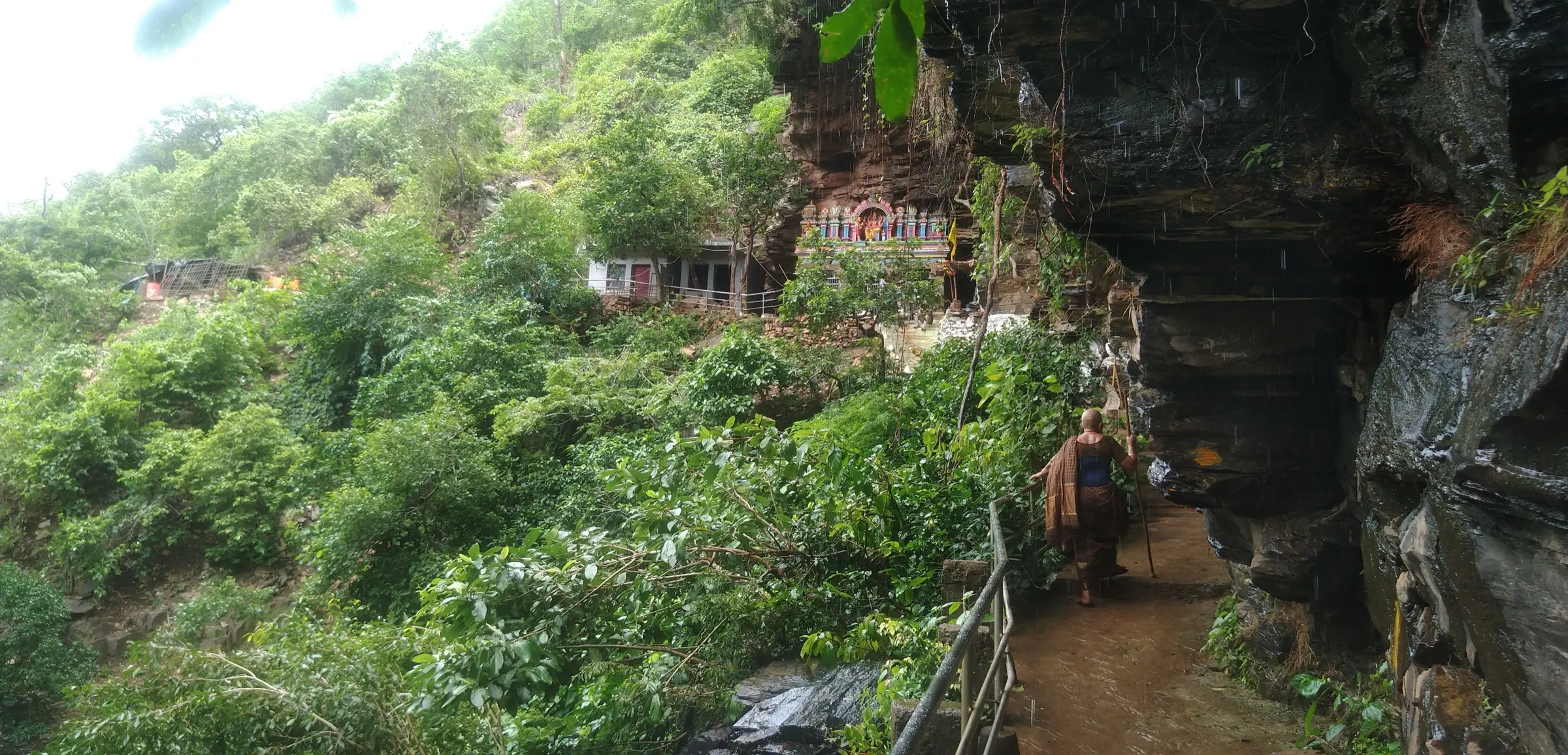 Railed rock path under an overhanging cliff leading to Jwala Narasimha temple on a forested hillside