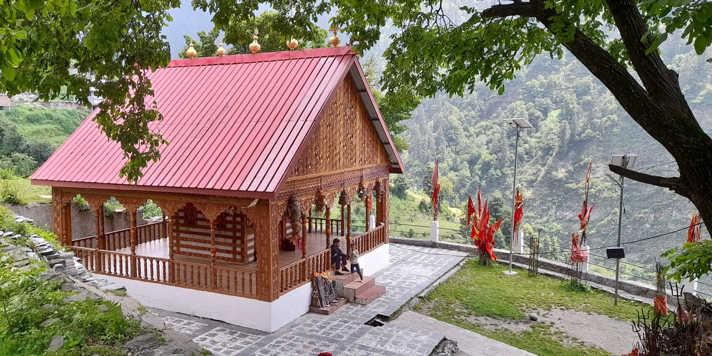 Kaali Mata temple with a red roof and carved wooden walls at Chanju in the Churah valley, near the start of the trek, with forested slopes behind