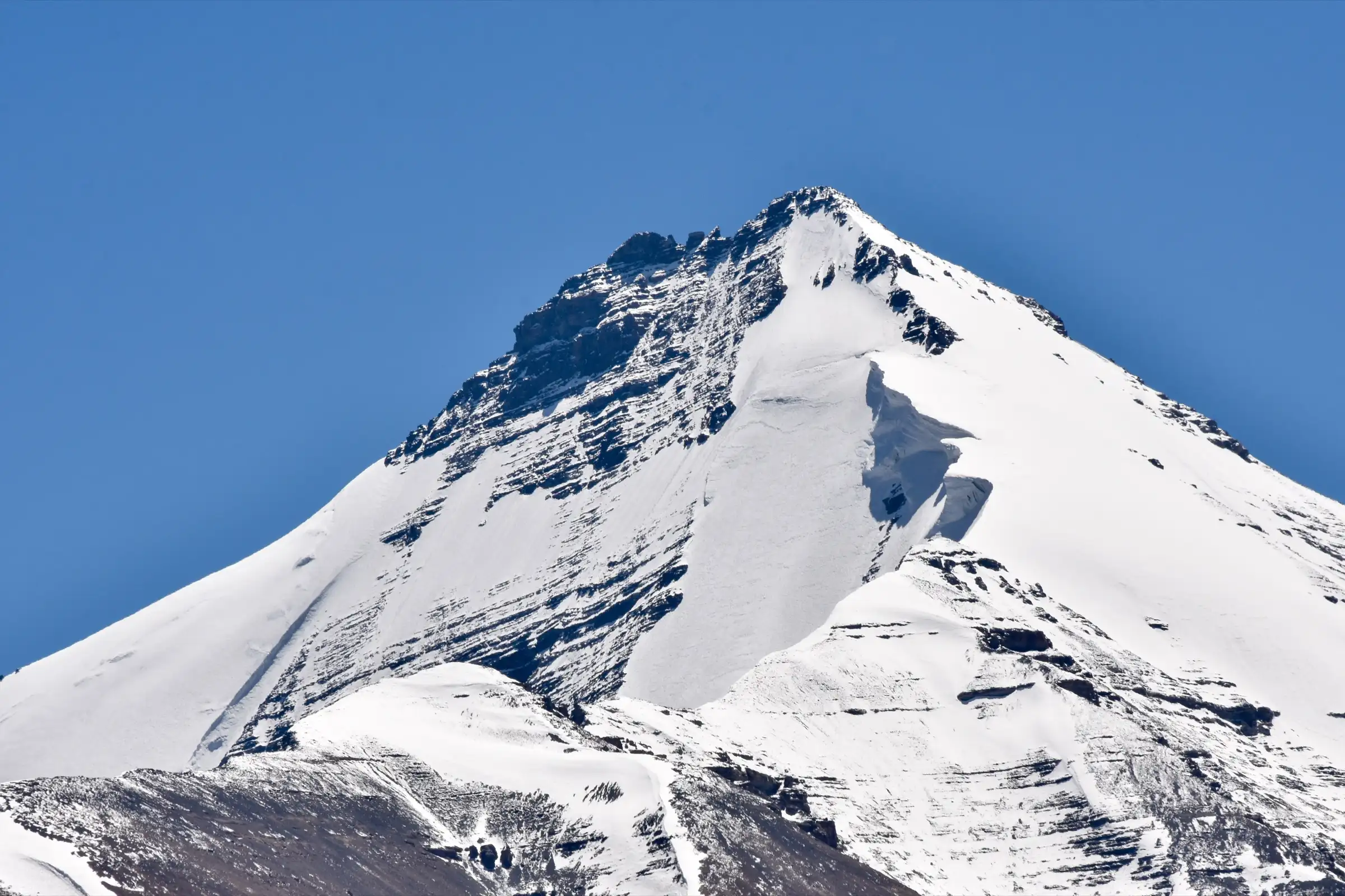 Snow-covered summit pyramid of Kanamo Peak against a blue sky, seen from the south above Kibber, Spiti