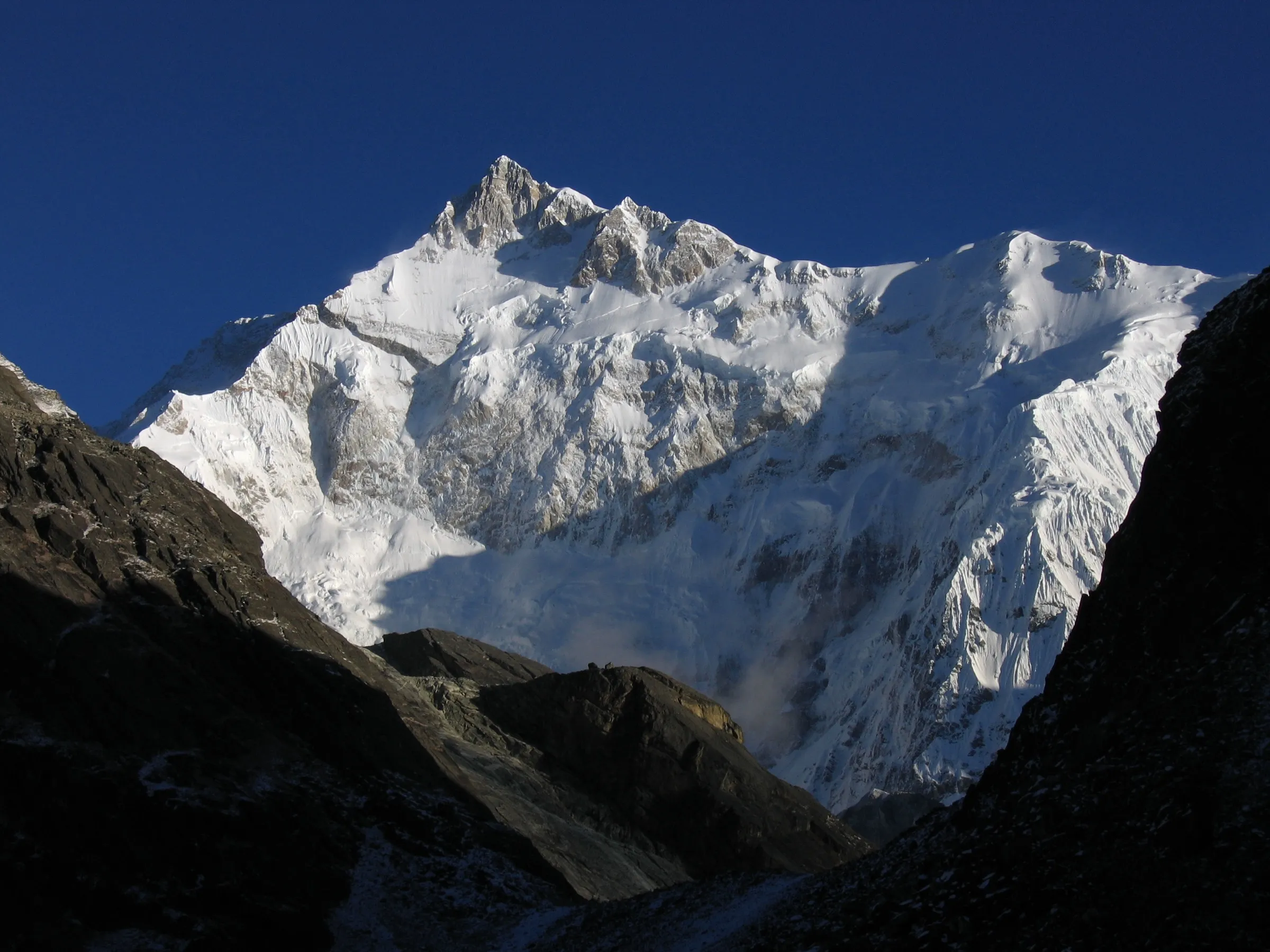 Snow and ice on the south-east face of Kanchenjunga under a deep blue sky, framed by dark rocky slopes near Goecha La