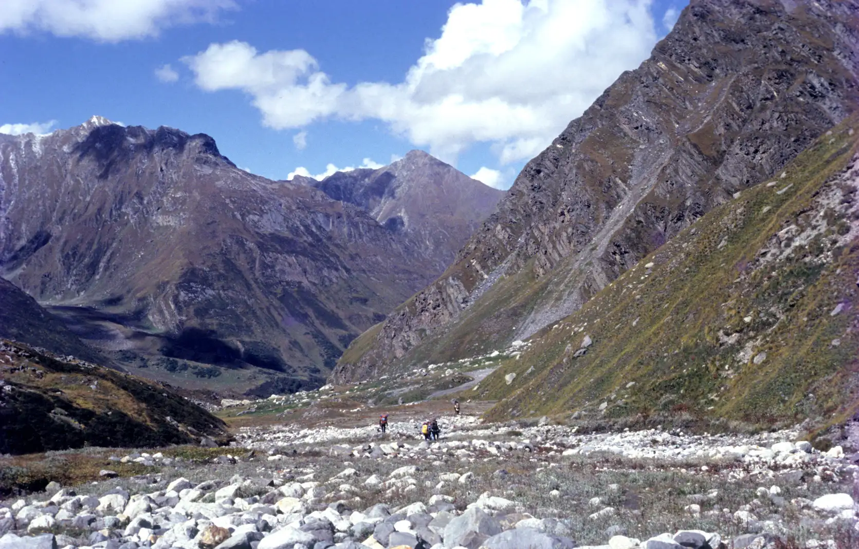 Trekkers crossing a boulder-strewn valley floor at the Kearkoti camping ground below rocky peaks
