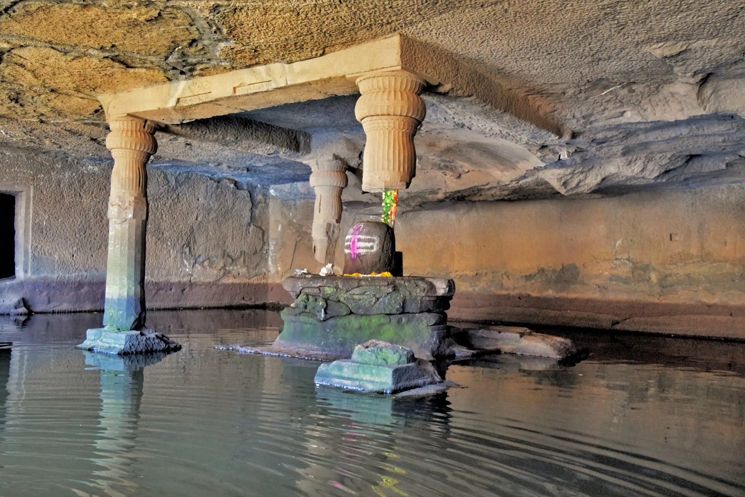 Shiva linga on a stone plinth surrounded by still water inside the pillared Kedareshwar cave