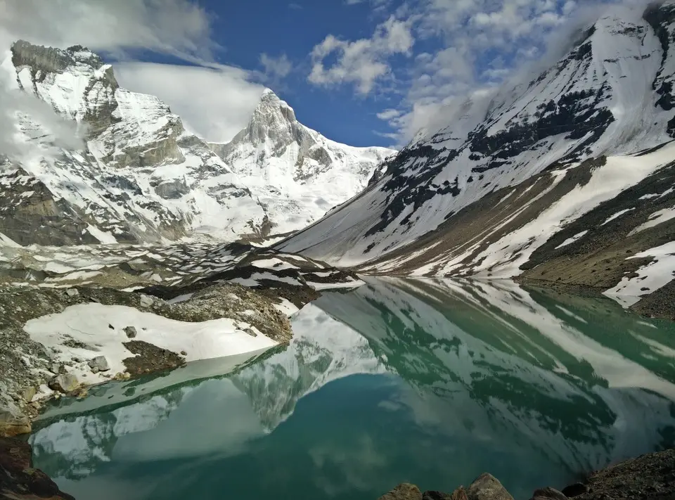 Snowy peaks and Thalay Sagar reflected in the still green water of Kedartal, with snow patches on the shore