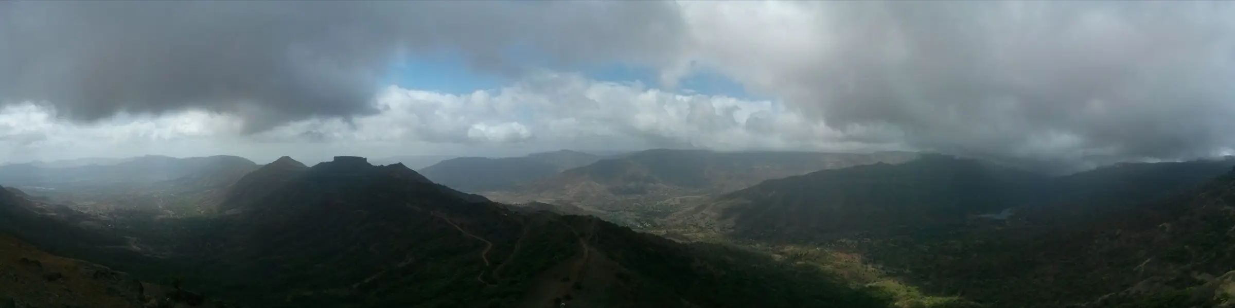 Panorama from Raireshwar with the flat-topped Kenjalgad fort on the left and a winding road below rain clouds