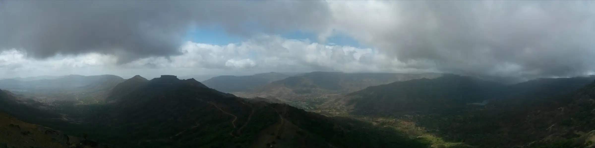 Panorama from Raireshwar with the flat-topped Kenjalgad fort on the left and a winding road below rain clouds