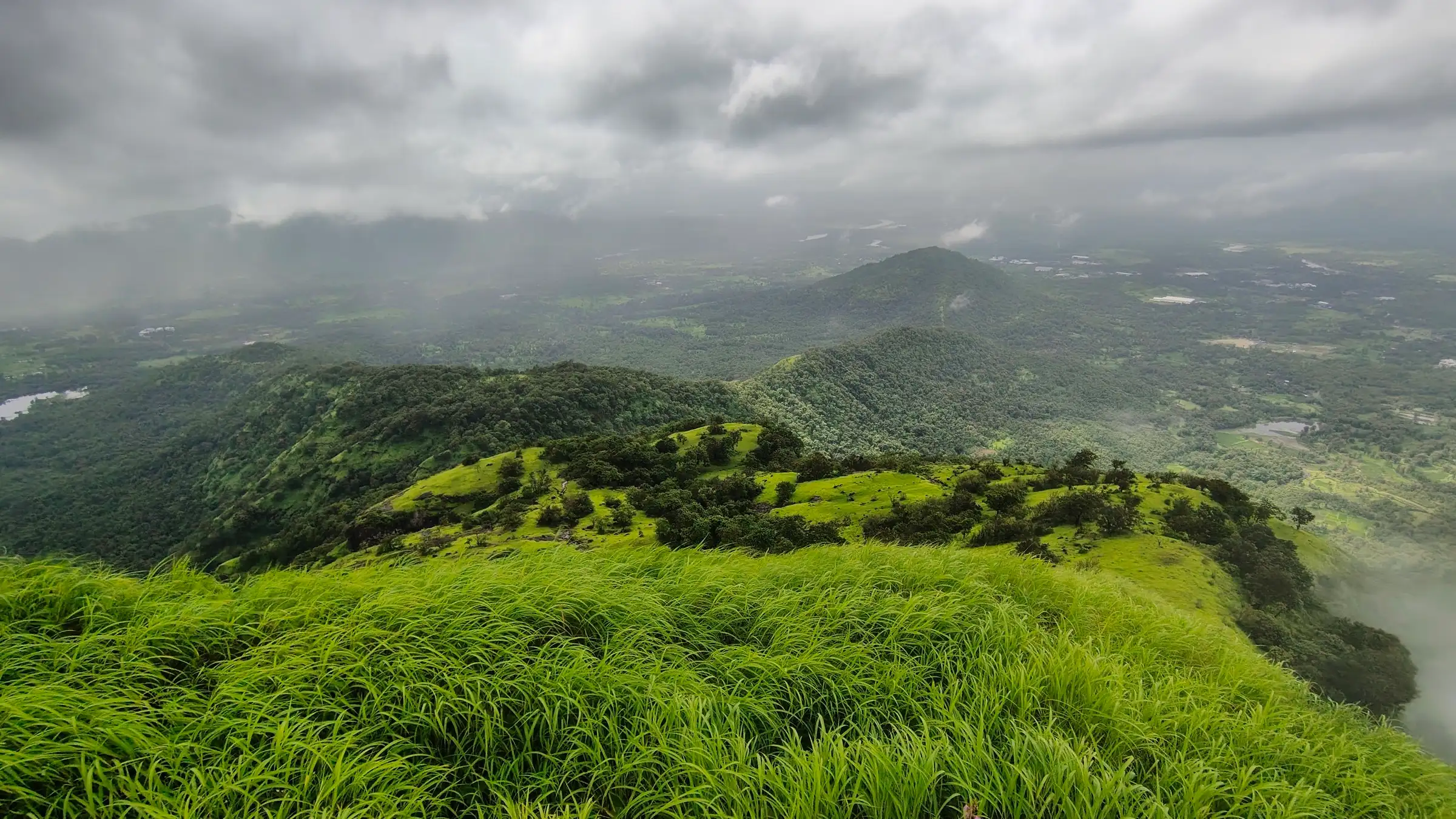 Green grassy ridge on Kohoj Fort looking over forested hills and lakes under monsoon clouds
