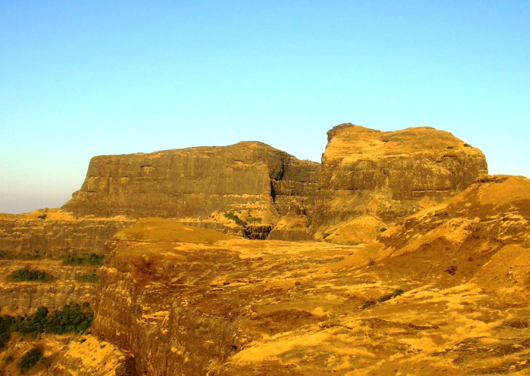 Sheer sunlit rock walls of Kulang and Madan forts seen from Alang Fort