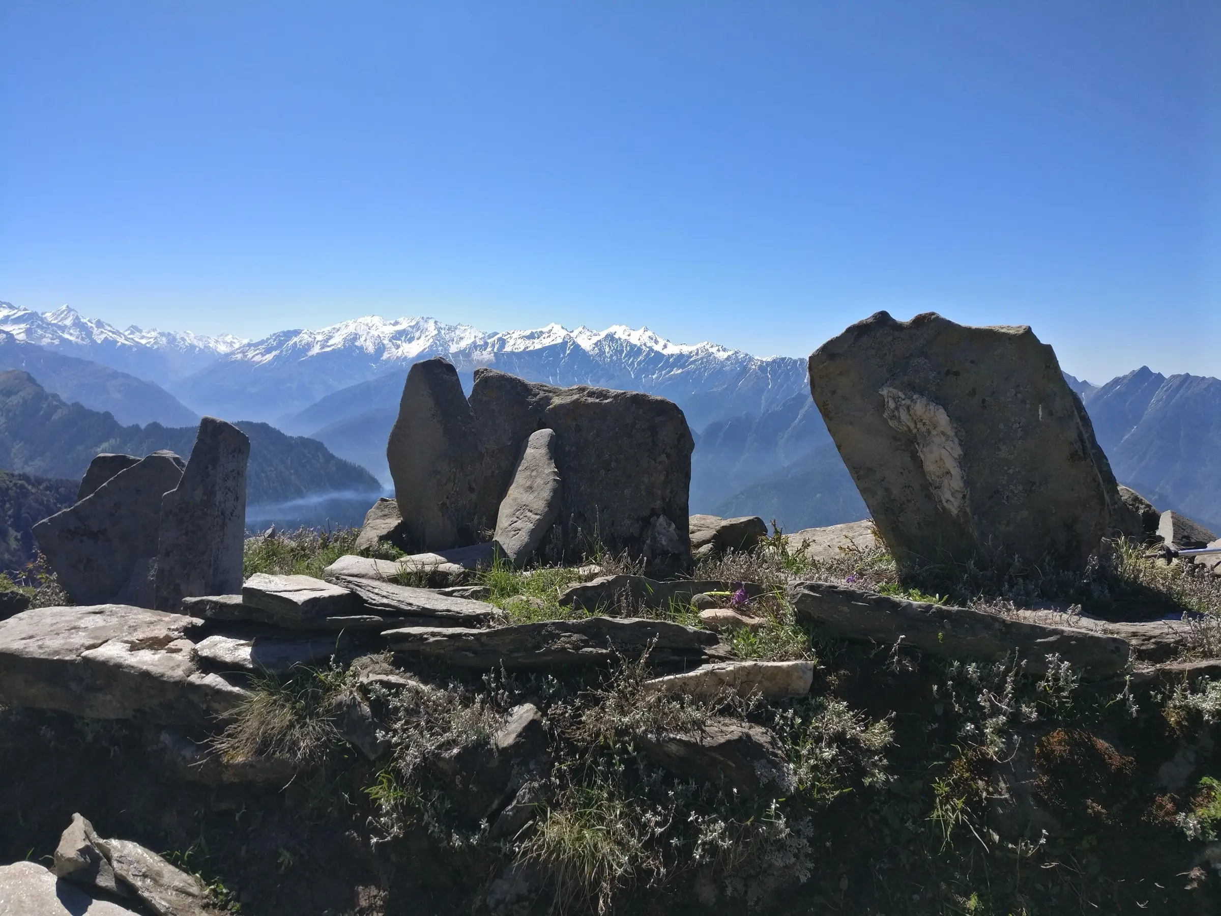 Upright standing stones on the Chanderkhani Pass ridge with snow-capped Kullu valley peaks behind