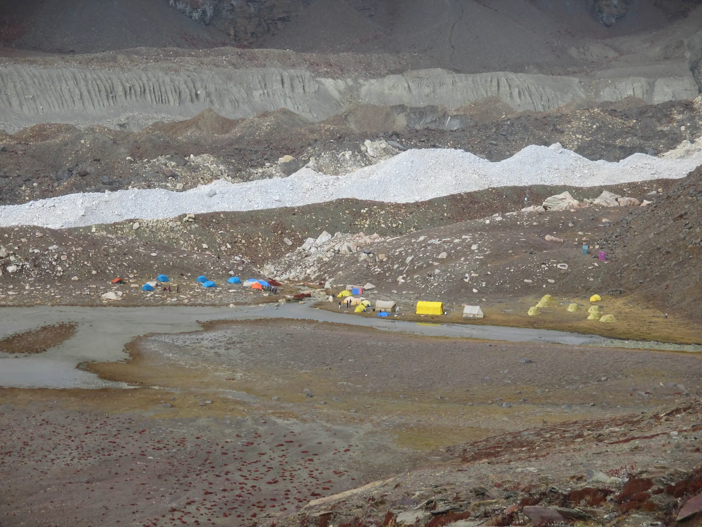 Trekkers' tents beside the shallow Vasuki Tal lake below the grey moraine and ice of the Chaturangi Glacier
