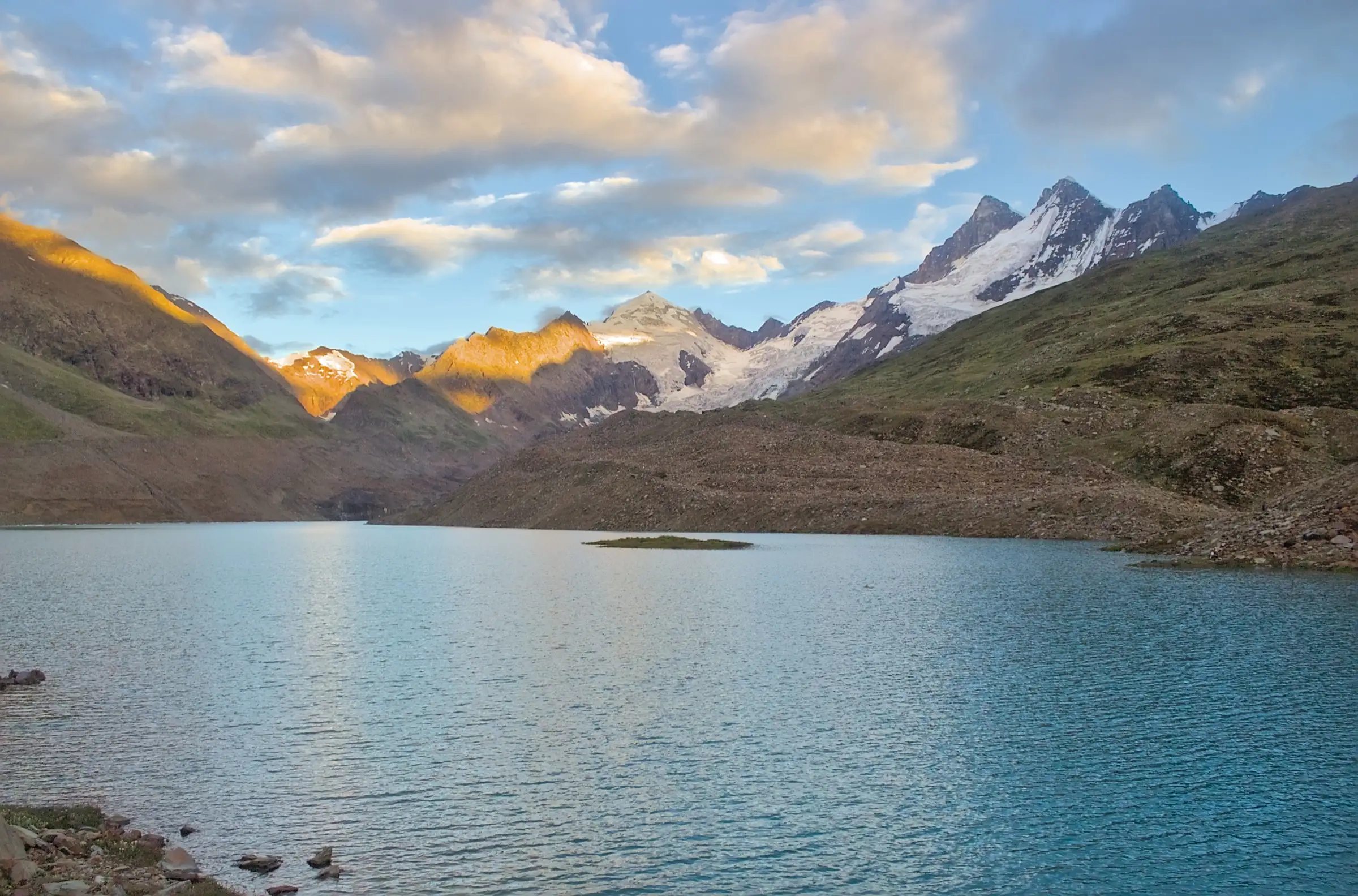 Blue Ghepan Lake with a small grassy island, below glaciated peaks lit by the evening sun