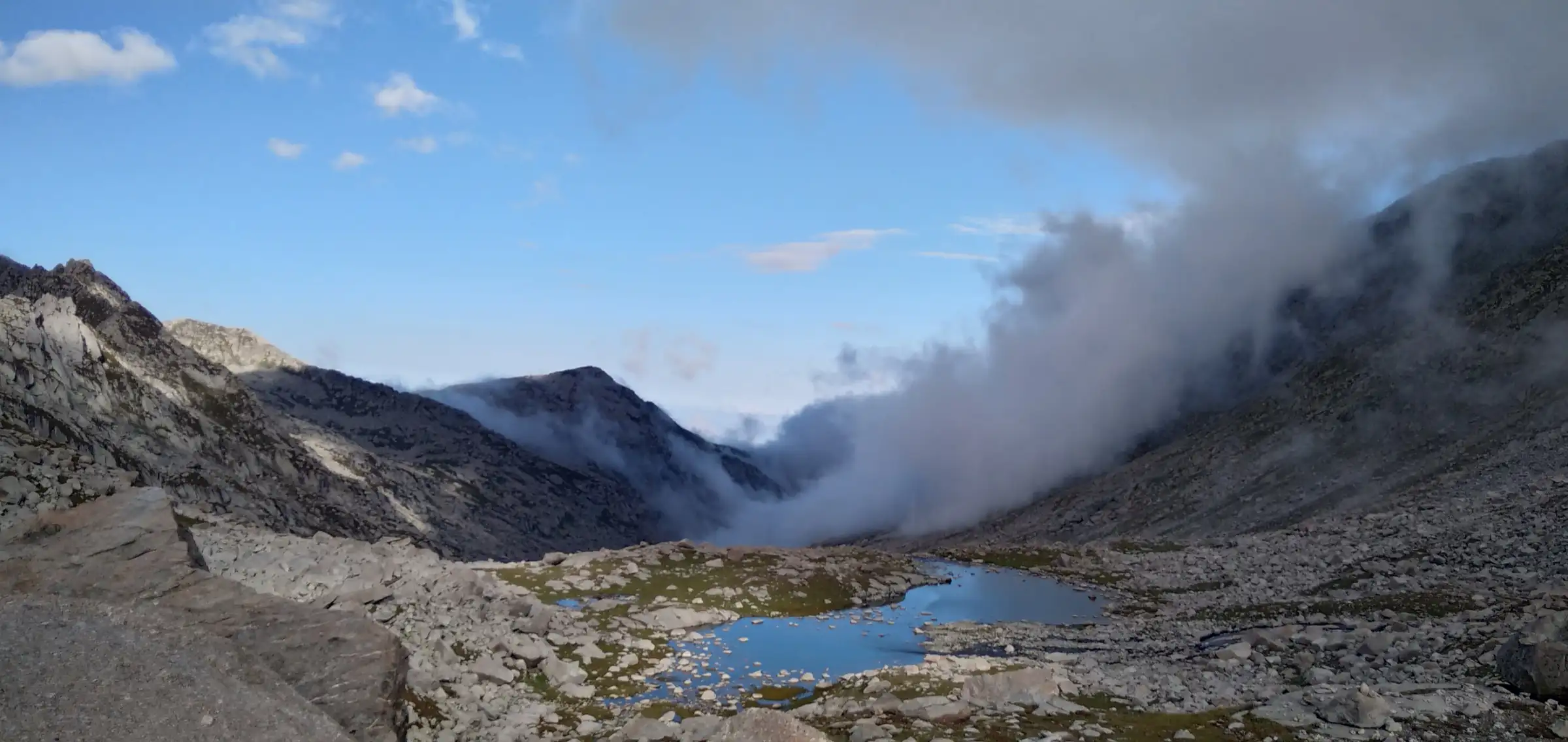 A small blue pool in the boulder basin the photographer captions as Lam Dal, with cloud rolling over the rocky Dhauladhar ridge