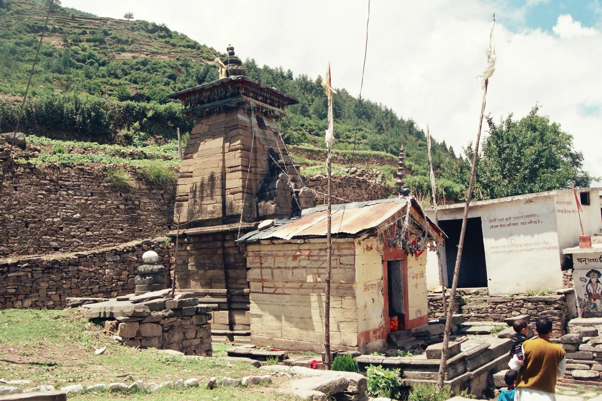 Old stone temple of Mata Nanda Devi with a small shrine beside it in Lata village, terraced green hillside behind