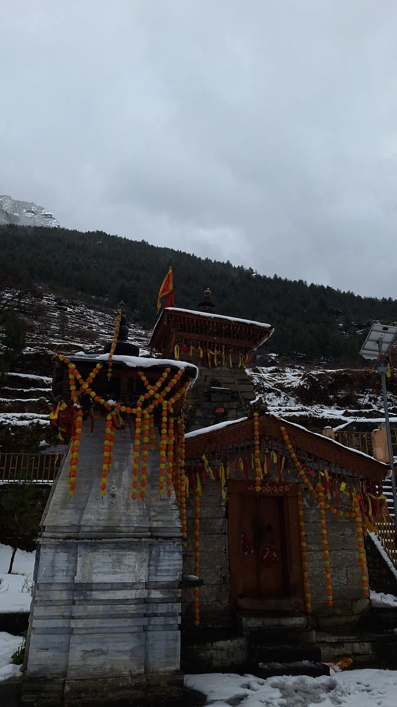 Nanda Devi temple in Lata village decorated with marigold garlands and a saffron flag, with fresh snow on the ground and forest behind