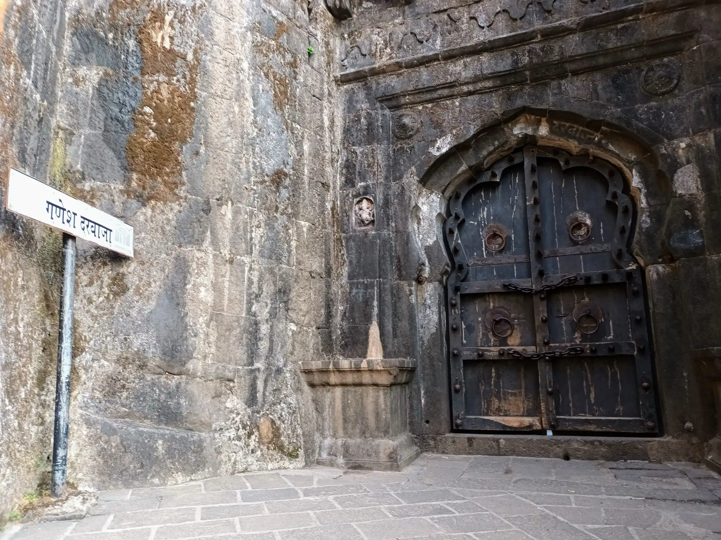 Studded wooden doors of Ganesh Darwaja at Lohagad Fort with a small carving of Bhagwan Ganesh beside the arch and a Marathi signboard