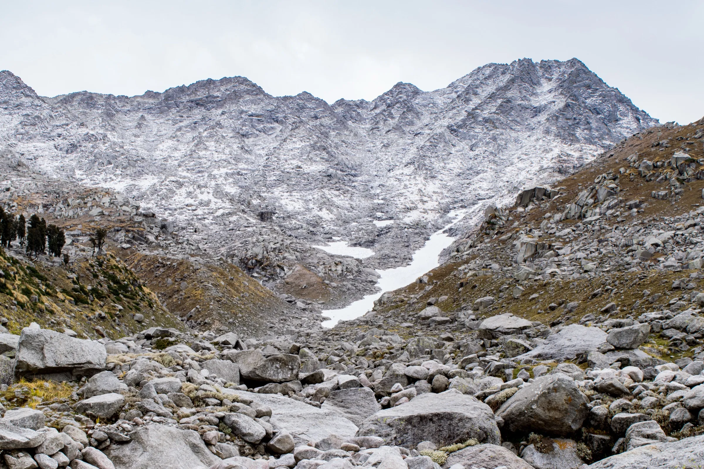 Snow-dusted granite wall of the Dhauladhar with a snow gully, looking up towards Indrahar Pass from the boulder fields above Laka Got