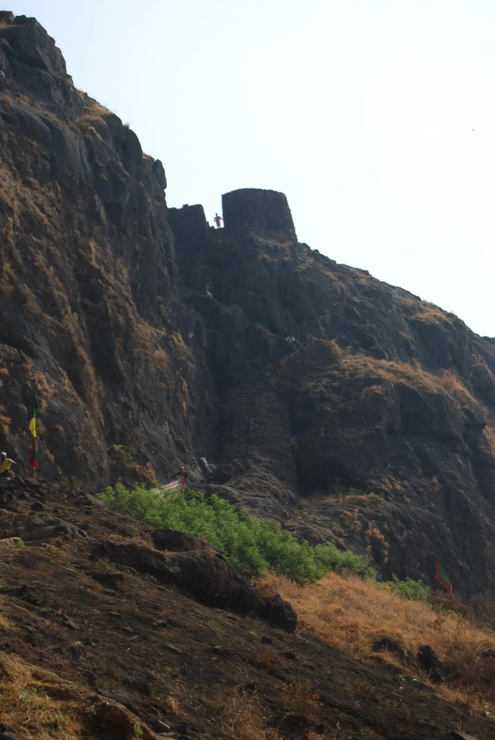 A round stone bastion of Malanggad's middle level perched on a steep rock face, with trekkers on the path below