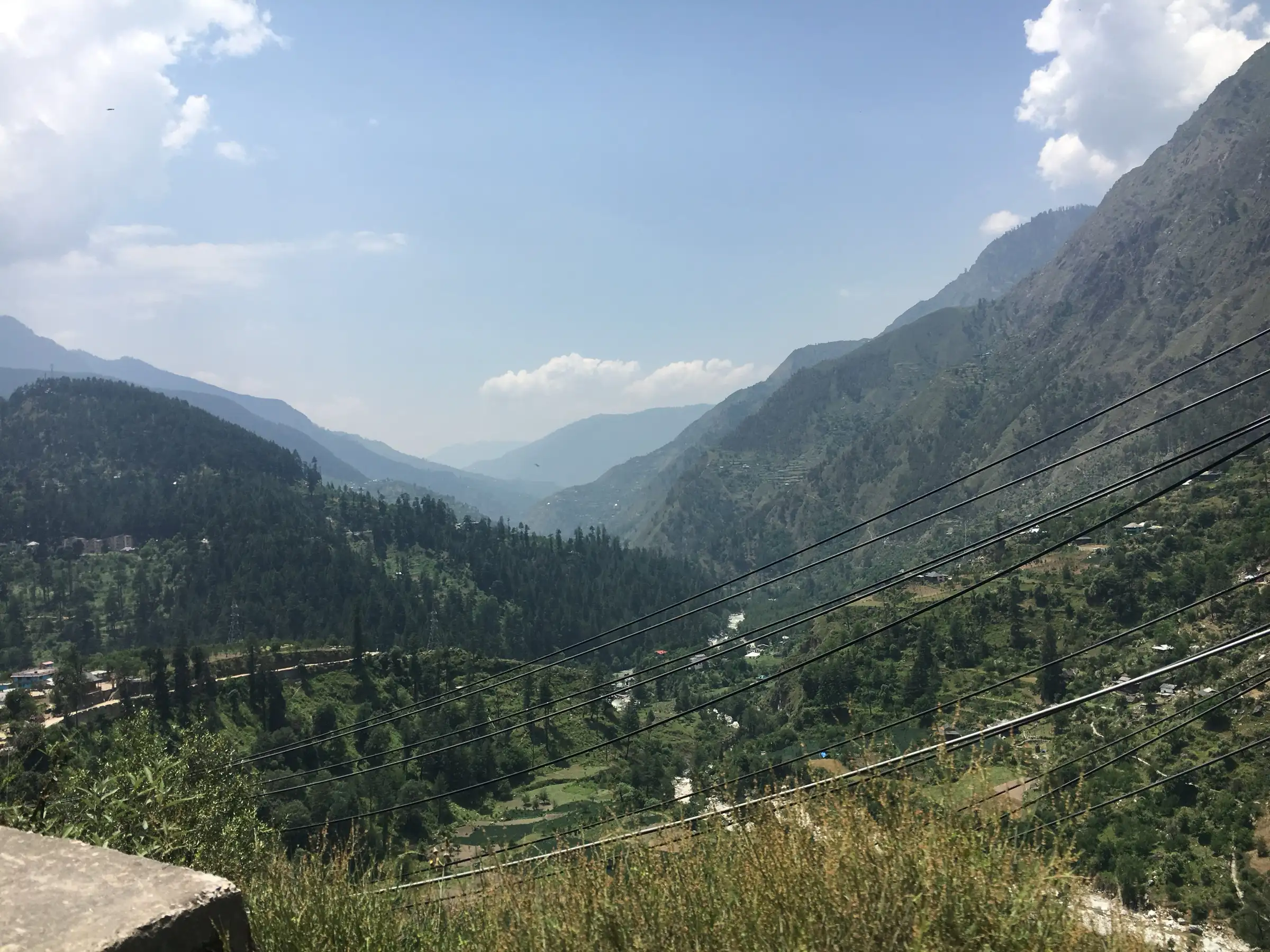 View down a forested valley with power lines, uploaded as a view from the Malana trek