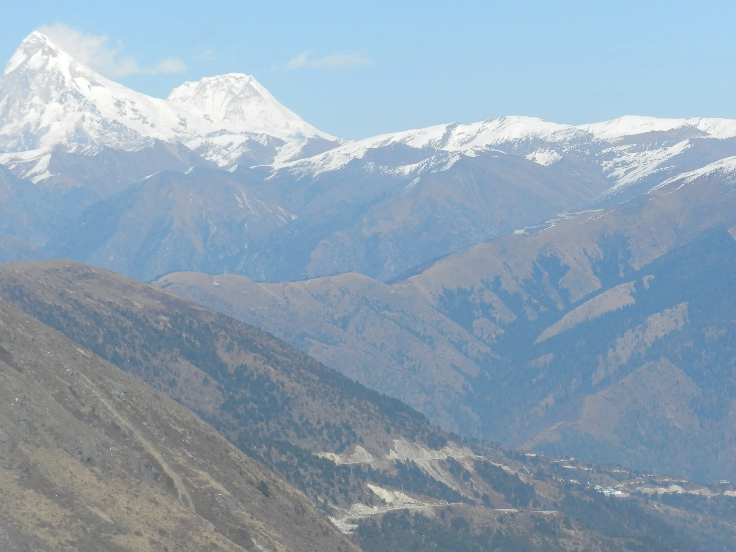 Snowy peaks of Indrasan and Deo Tibba seen from Malana village across the brown hills, a view of the range near the trek, not the trail itself